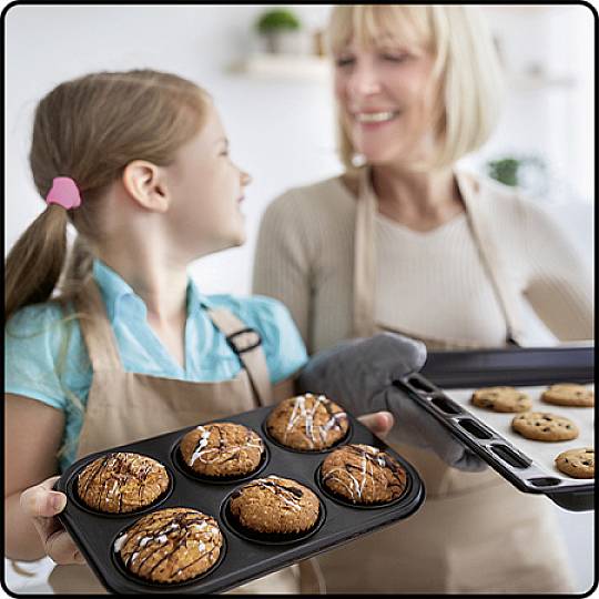 Ein Mädchen und eine Frau backen zusammen. Das Mädchen hält ein Tablett mit Muffins, die Frau hält ein Blech mit Keksen. Sie lachen.
