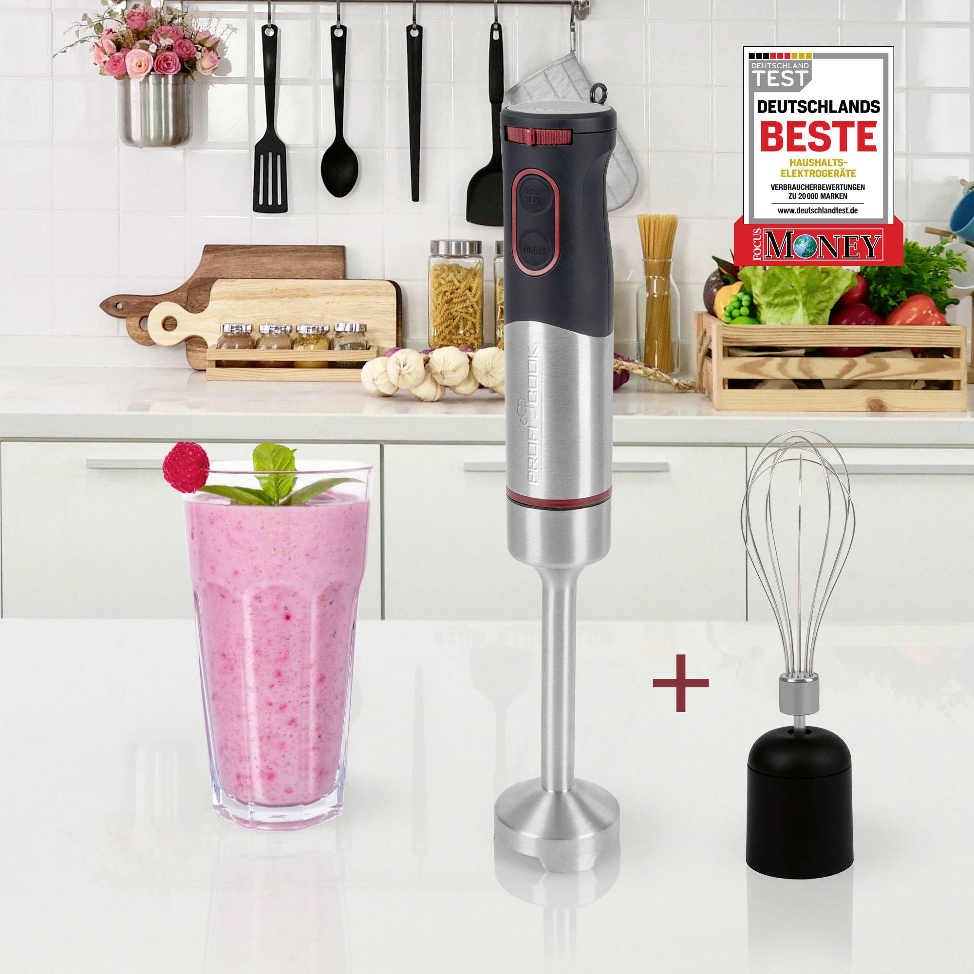 Ein Pürierstab steht auf einer Küchentheke neben einem Glas Erdbeer-Smoothie. Dahinter ein Schneebesen und Küchenutensilien.