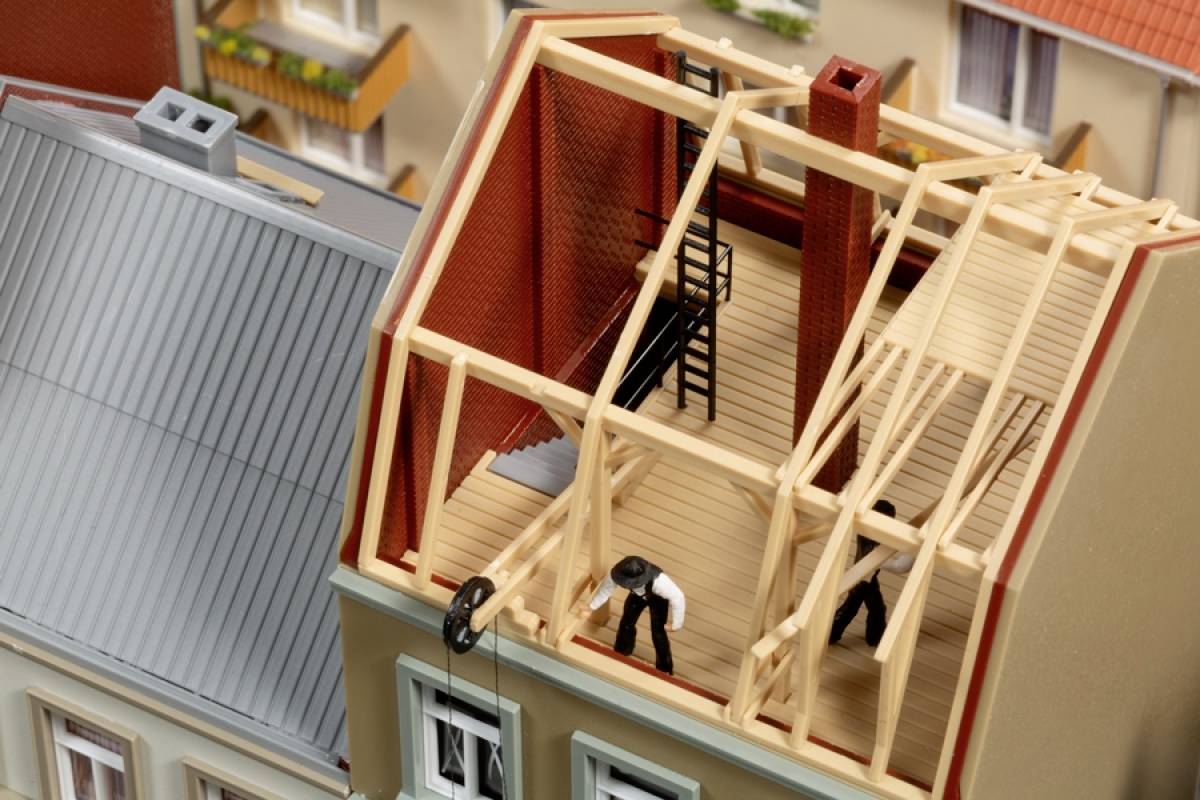 Ein Modellhaus mit teilweise offenem Dach zeigt eine Dachkonstruktion aus Holz. Zwei Figuren arbeiten am Bau des Dachs.
