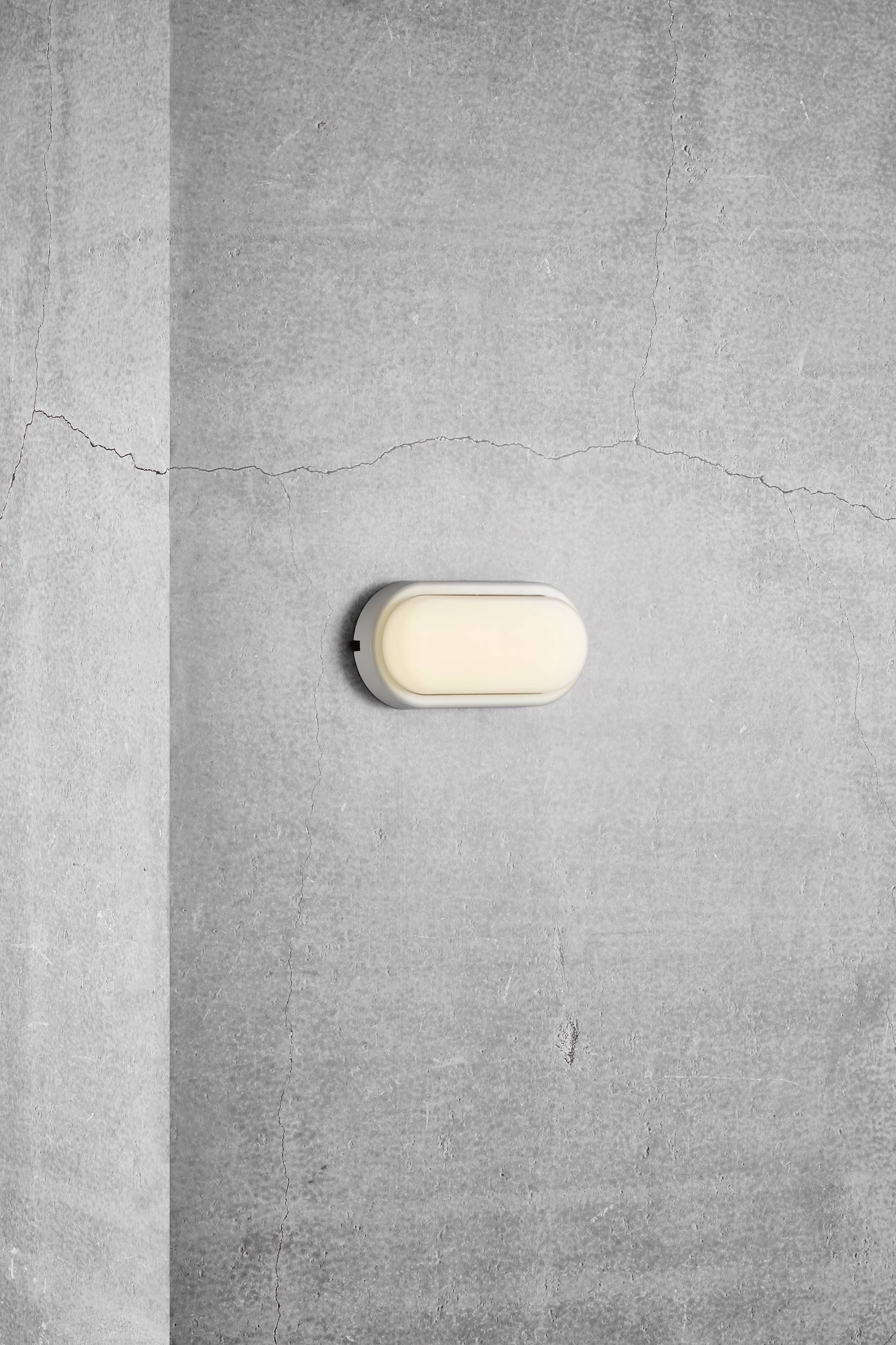 Graue Betonwand mit einer ovalen, eingeschalteten Wandlampe in der Mitte. Die Wand hat einen sichtbaren Riss oberhalb der Lampe.