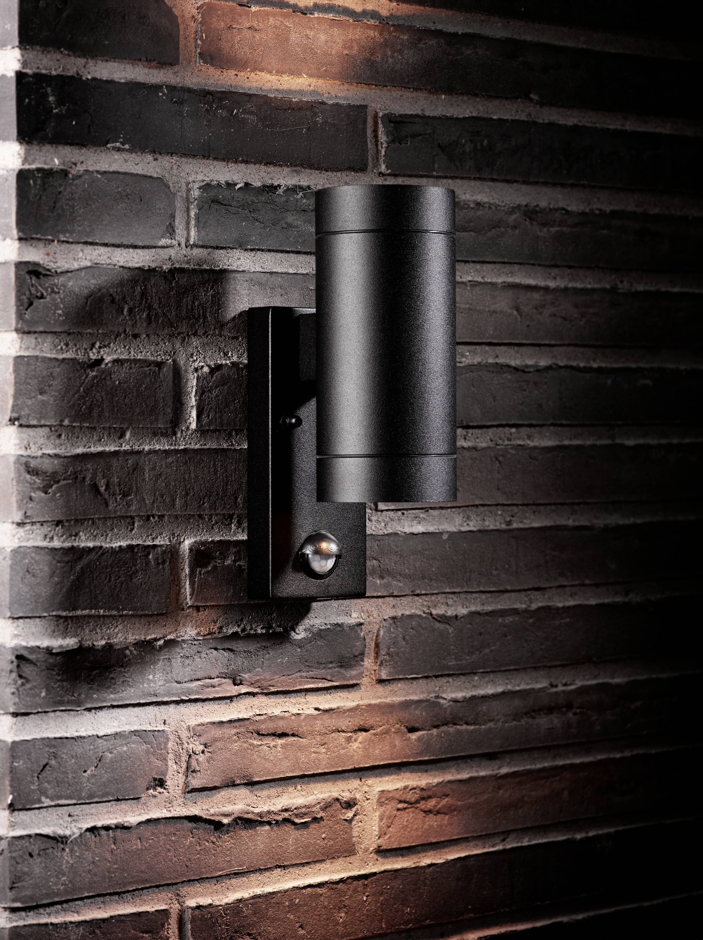 Schwarze Wandleuchte aus Metall montiert an einer Ziegelwand, beleuchtet von oben und unten, bietet dekorative Außenbeleuchtung.