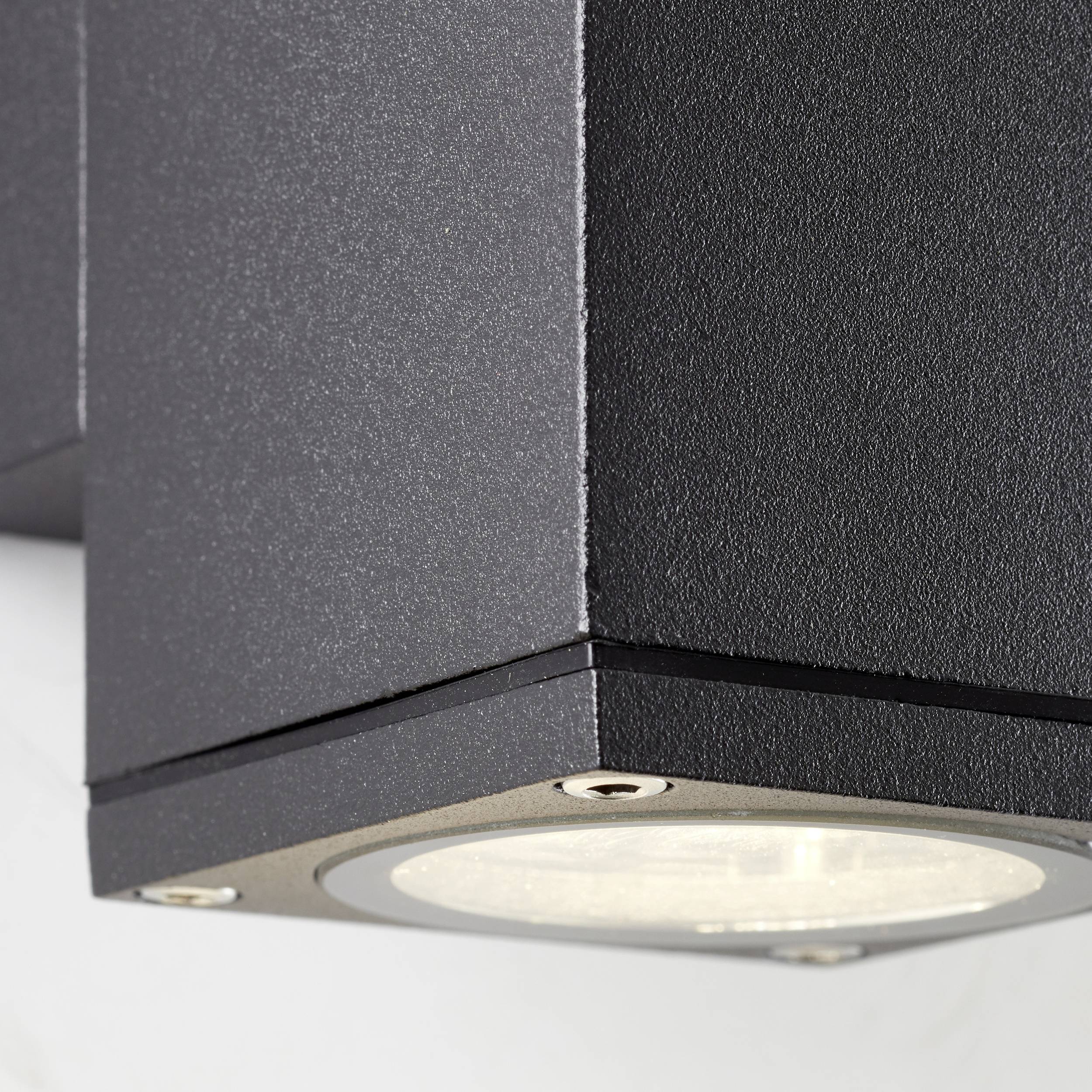 Schwarze, sechseckige Außen-Wandlampe mit klarer Glasabdeckung, an einer weißen Oberfläche montiert.