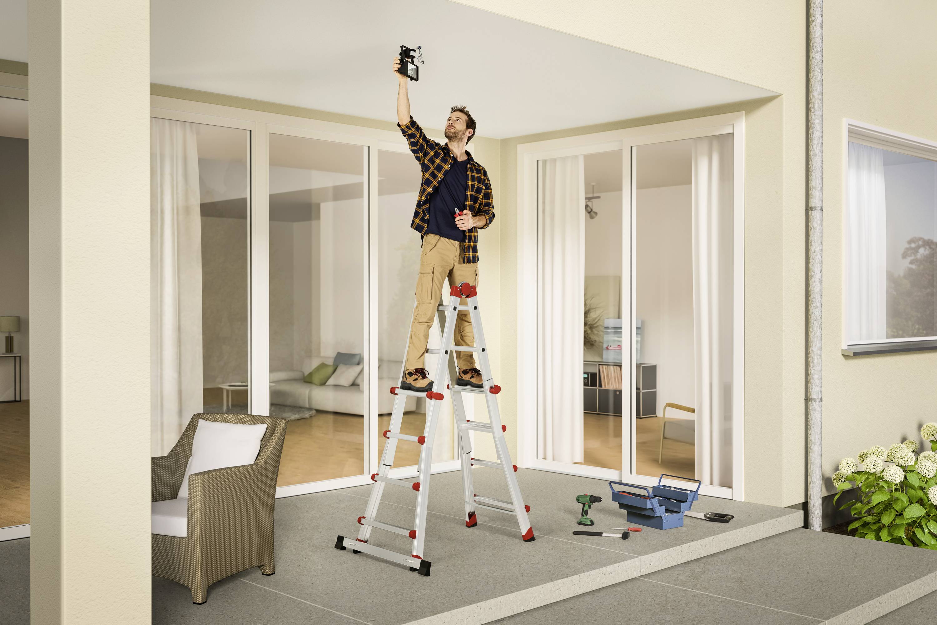 Ein Mann steht auf einer Leiter und installiert eine Lampe an der Decke eines überdachten Außenbereichs. Werkzeug liegt auf dem Boden.