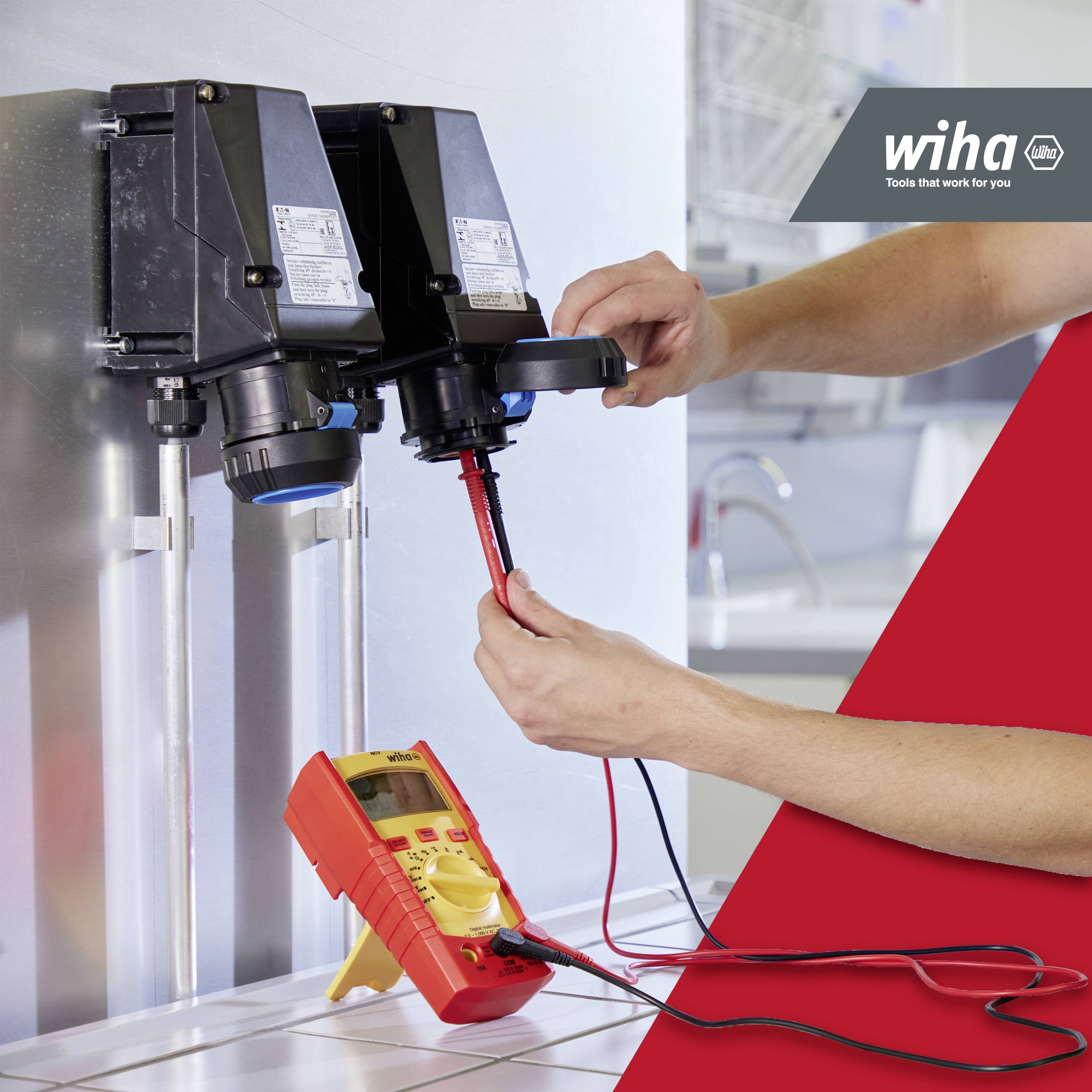 Eine Person verwendet ein Multimeter, um elektrische Anschlüsse an zwei Geräten zu prüfen. Oben rechts ist das Logo einer Handwerksfirma.