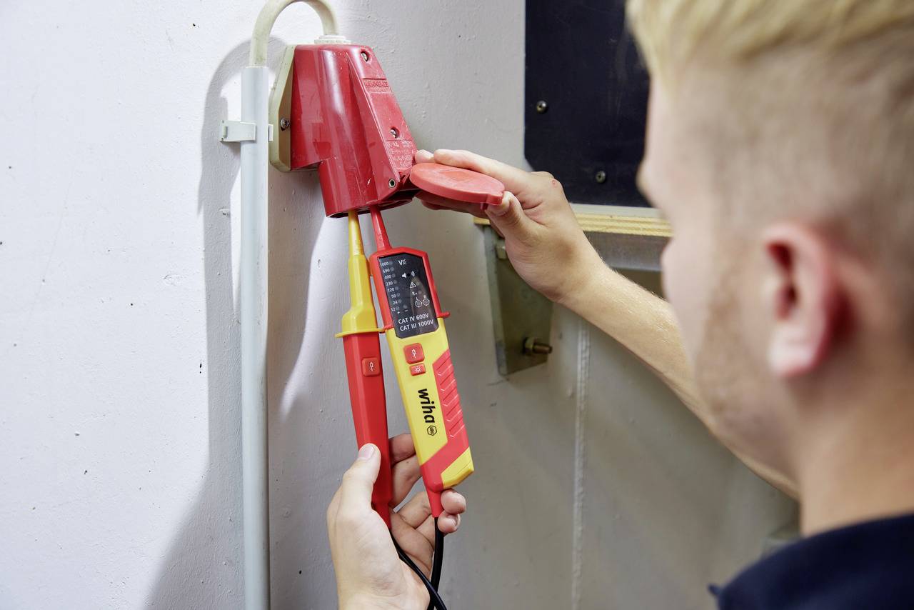 Ein Elektriker prüft mit einem Spannungsprüfer den elektrischen Anschluss in einer roten Steckdose.