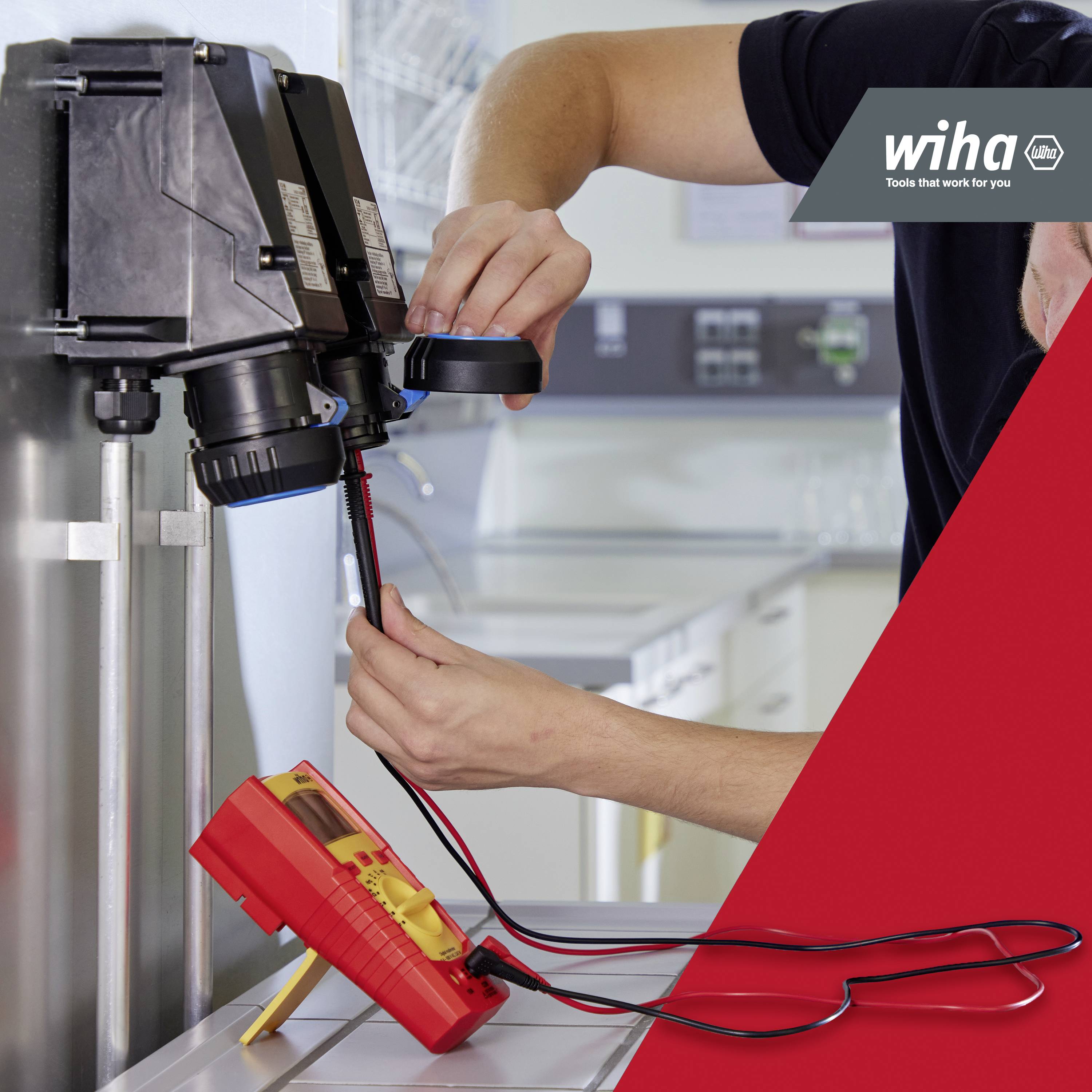 Ein Handwerker benutzt ein Spannungsprüfer an einer elektrischen Anlage in einer Werkstatt. Das Logo 'Wiha' ist sichtbar.