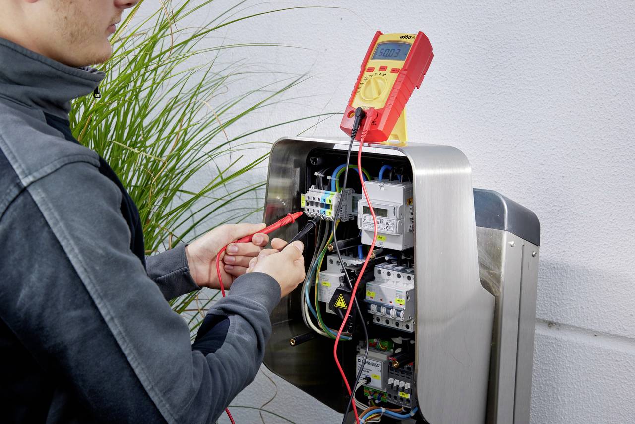 Eine Person prüft elektrische Verbindungen in einer geöffneten Schalttafel mit einem Multimeter.