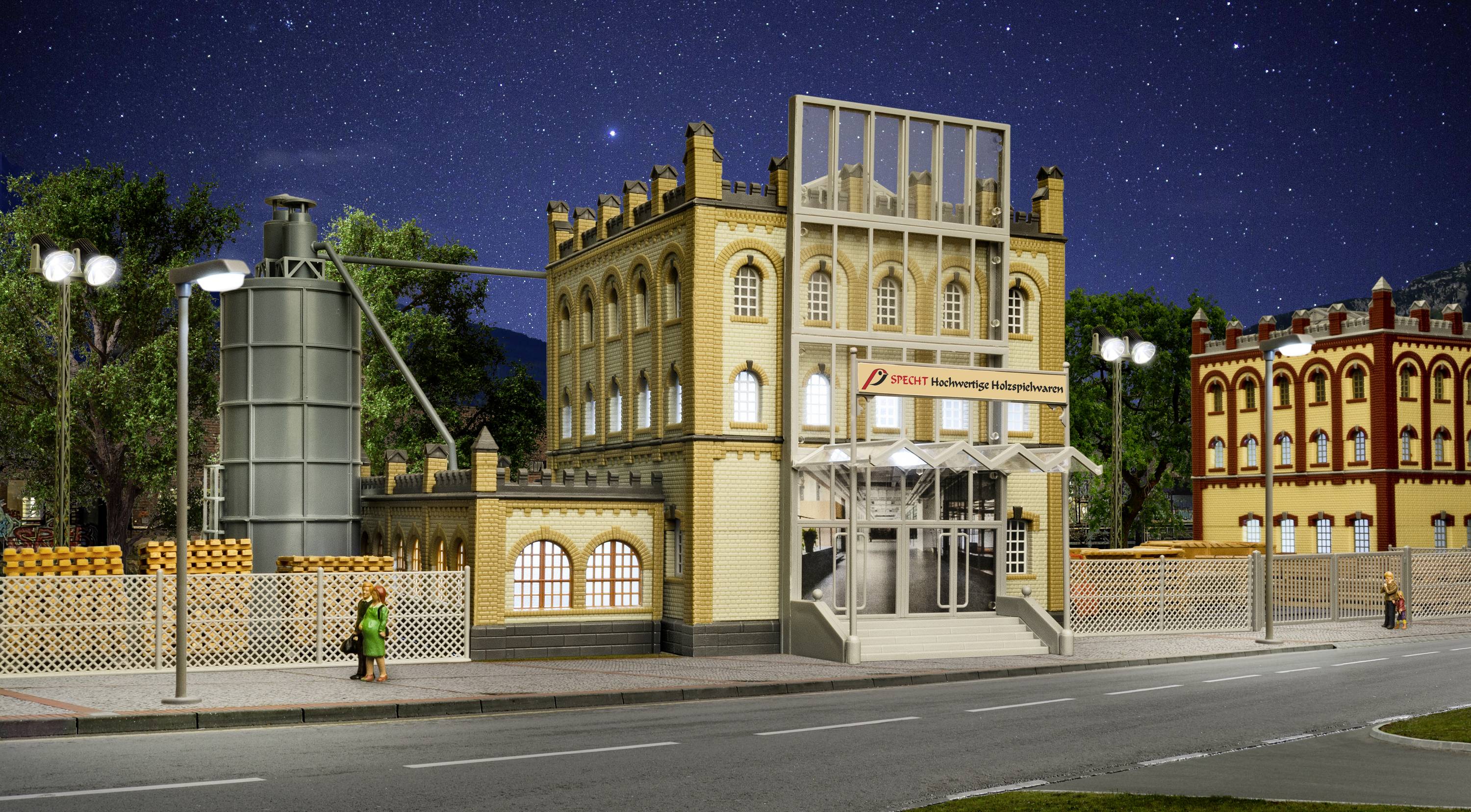 Ein beleuchtetes Modell eines historischen Bahnhofs bei Nacht. Im Vordergrund sind Gehwege und eine Person zu sehen.