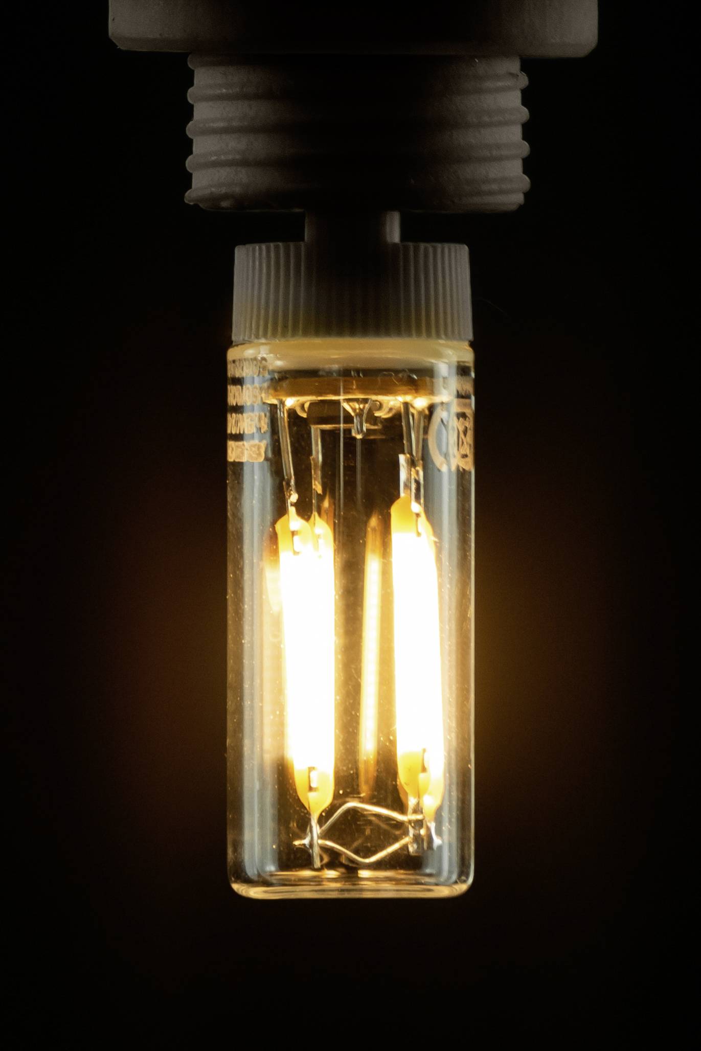 Eine leuchtende Glühbirne hängt von einer Fassung. Der Glühdraht ist sichtbar und strahlt warmes, gelbliches Licht aus.