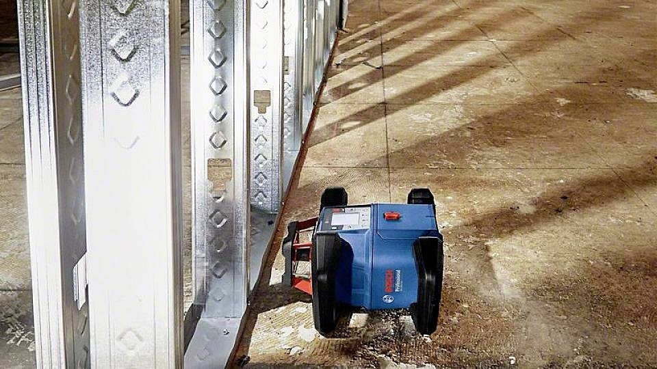 Ein blauer Roboter bewegt sich entlang einer Metallwand in einer Baustelle, möglicherweise zur Vermessung oder Inspektion.