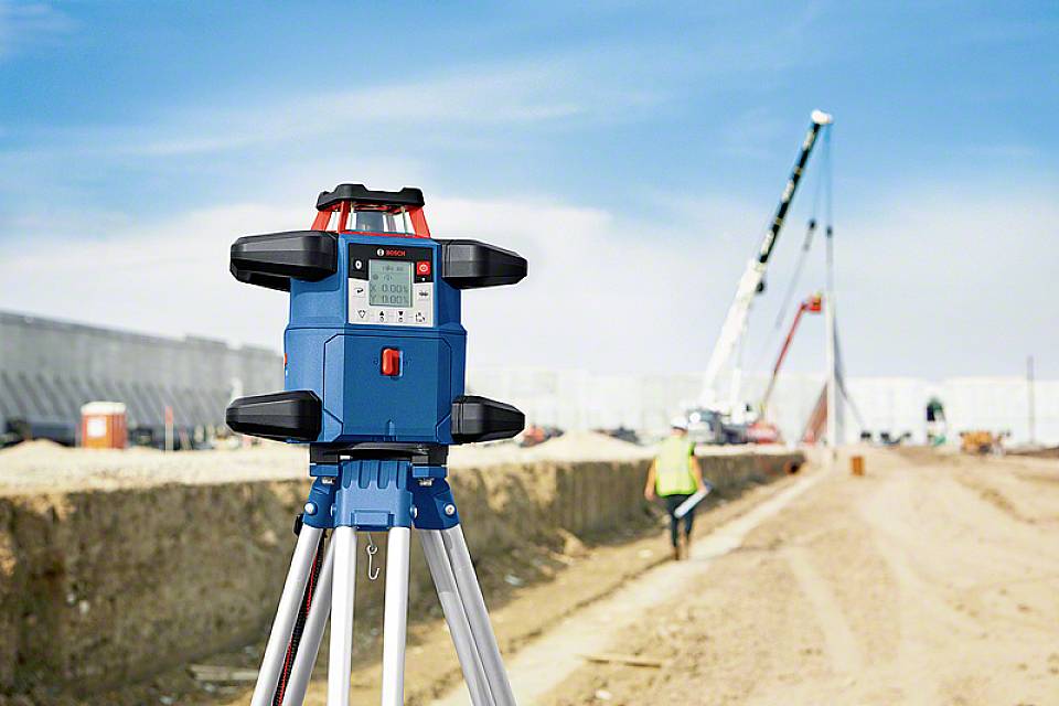 Vermessungsgerät auf Baustelle mit Kran im Hintergrund; das Gerät wird zur präzisen Ausrichtung und Messung von Distanzen verwendet.