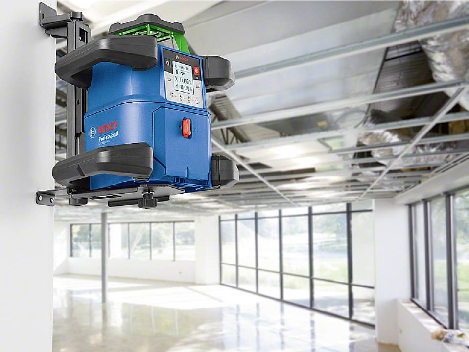 Ein blauer Laser-Nivelliergerät ist an einer weißen Wand in einem modernen, leeren Raum mit großen Fenstern montiert.