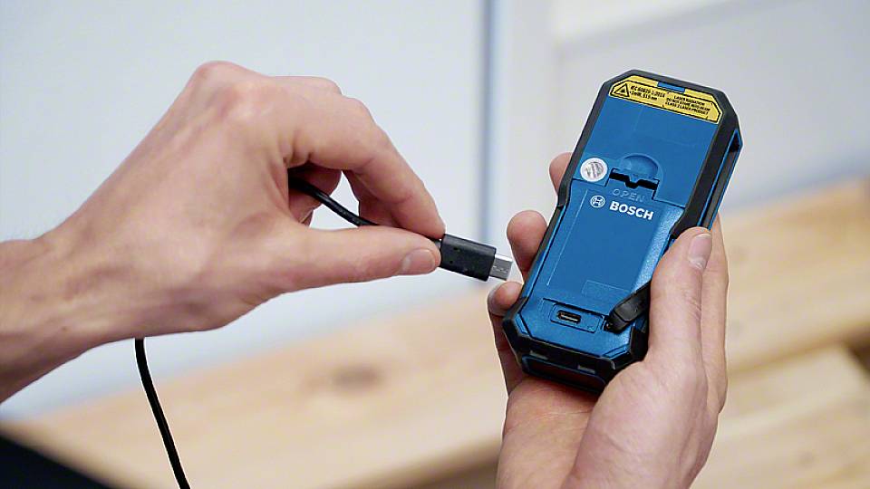 Eine Hand hält ein blaues Elektrowerkzeug von Bosch, während die andere einen Ladekabelstecker in das Gerät einführt.