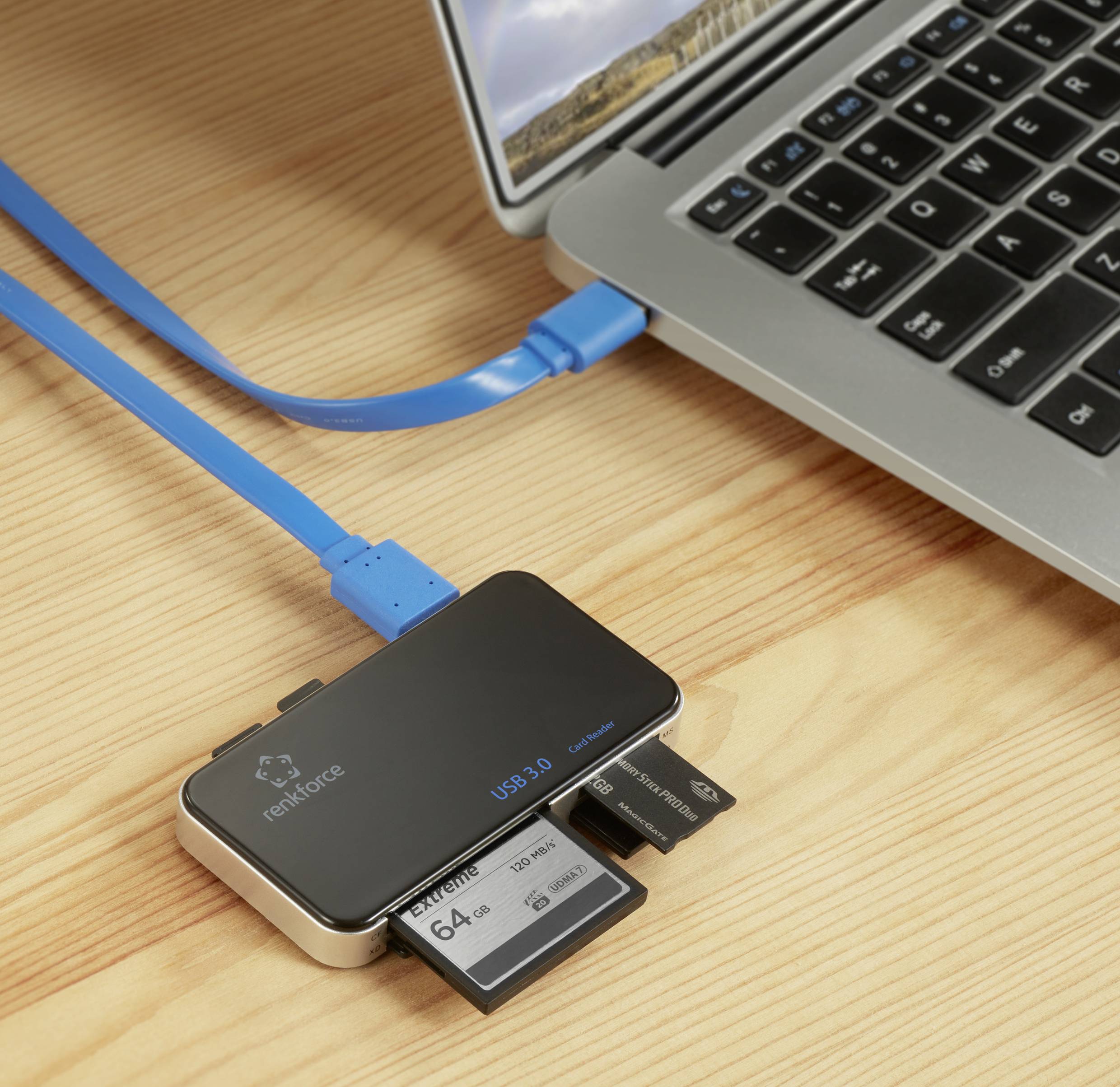 Ein USB-Hub mit drei eingesteckten Speicherkarten ist über ein blaues Kabel mit einem Laptop auf einem Holztisch verbunden.