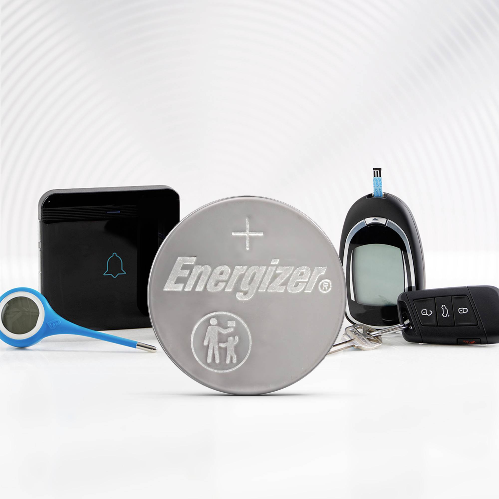 Eine silberne Energizer-Knopfzelle liegt im Vordergrund, umgeben von elektronischen Geräten wie einem Thermometer, einer Fernbedienung und einem Blutzuckermessgerät.