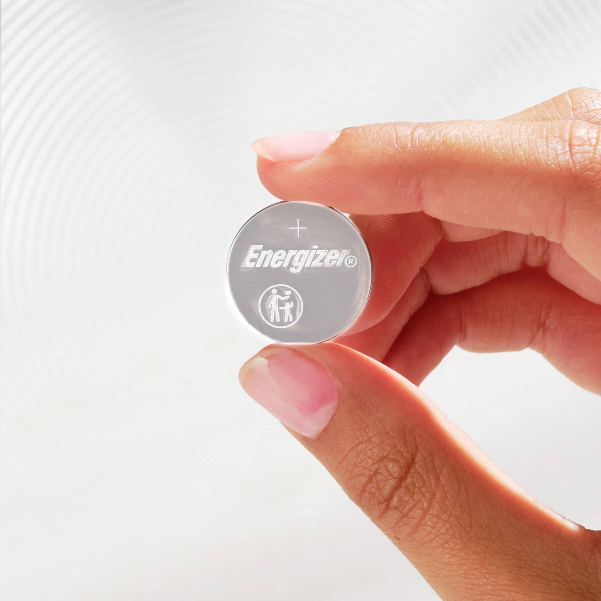 Finger hält eine runde Energizer-Batterie mit positivem Polsymbol und Sicherheitswarnung. Hintergrund hell und verschwommen.