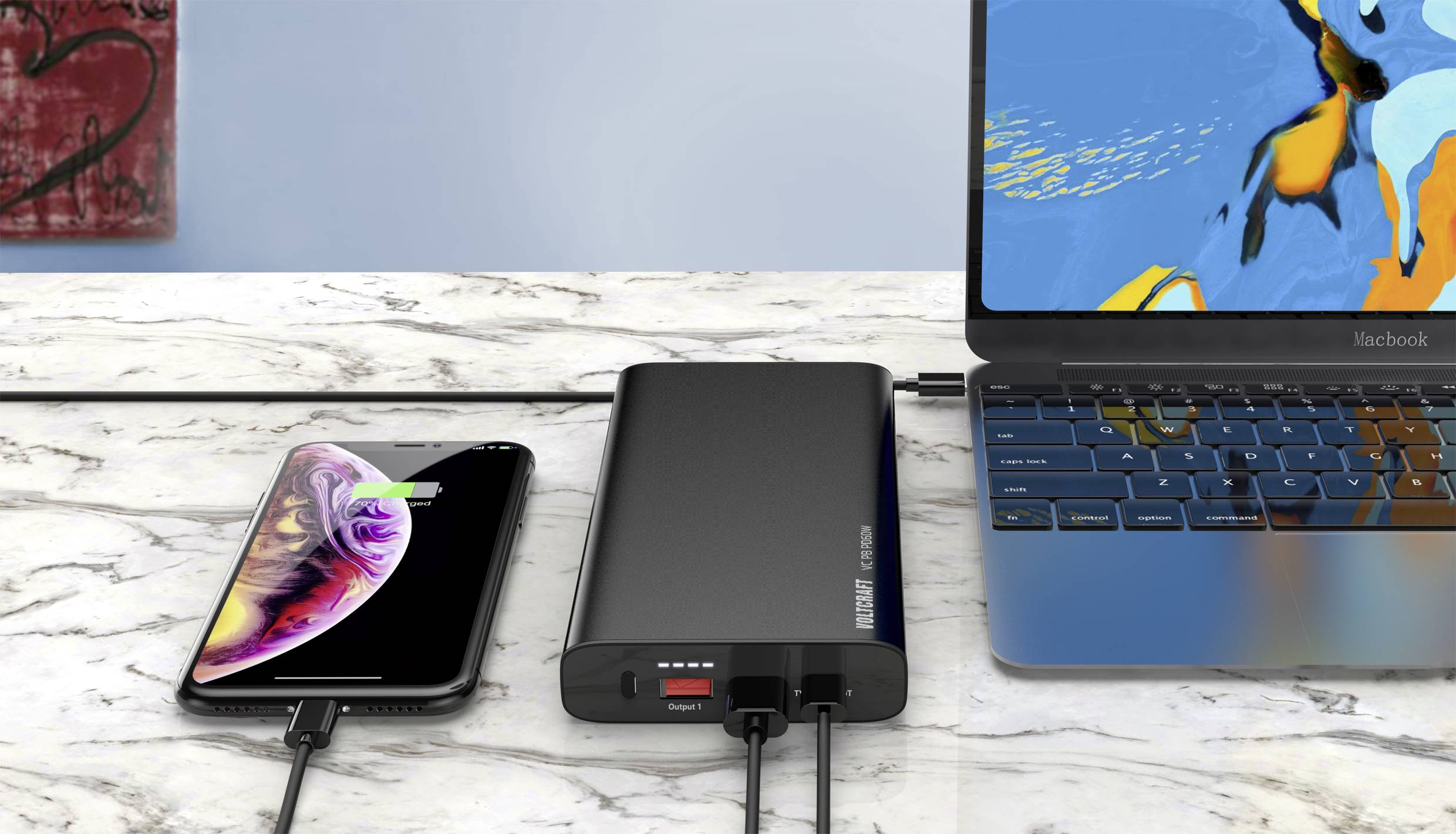 Ein Smartphone und ein Laptop laden gleichzeitig mit einer Powerbank auf einem Marmortisch auf. Das Smartphone zeigt einen Ladebildschirm.