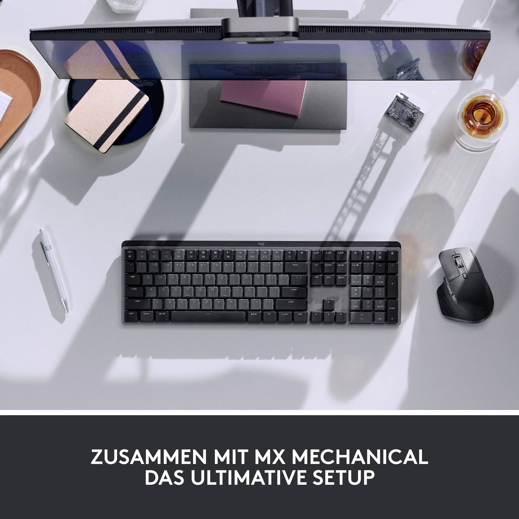 Arbeitsplatzansicht von oben mit Tastatur, Monitor, Maus und Drinks auf einem weißen Schreibtisch. Text: 'Zusammen mit MX Mechanical das ultimative Setup'.