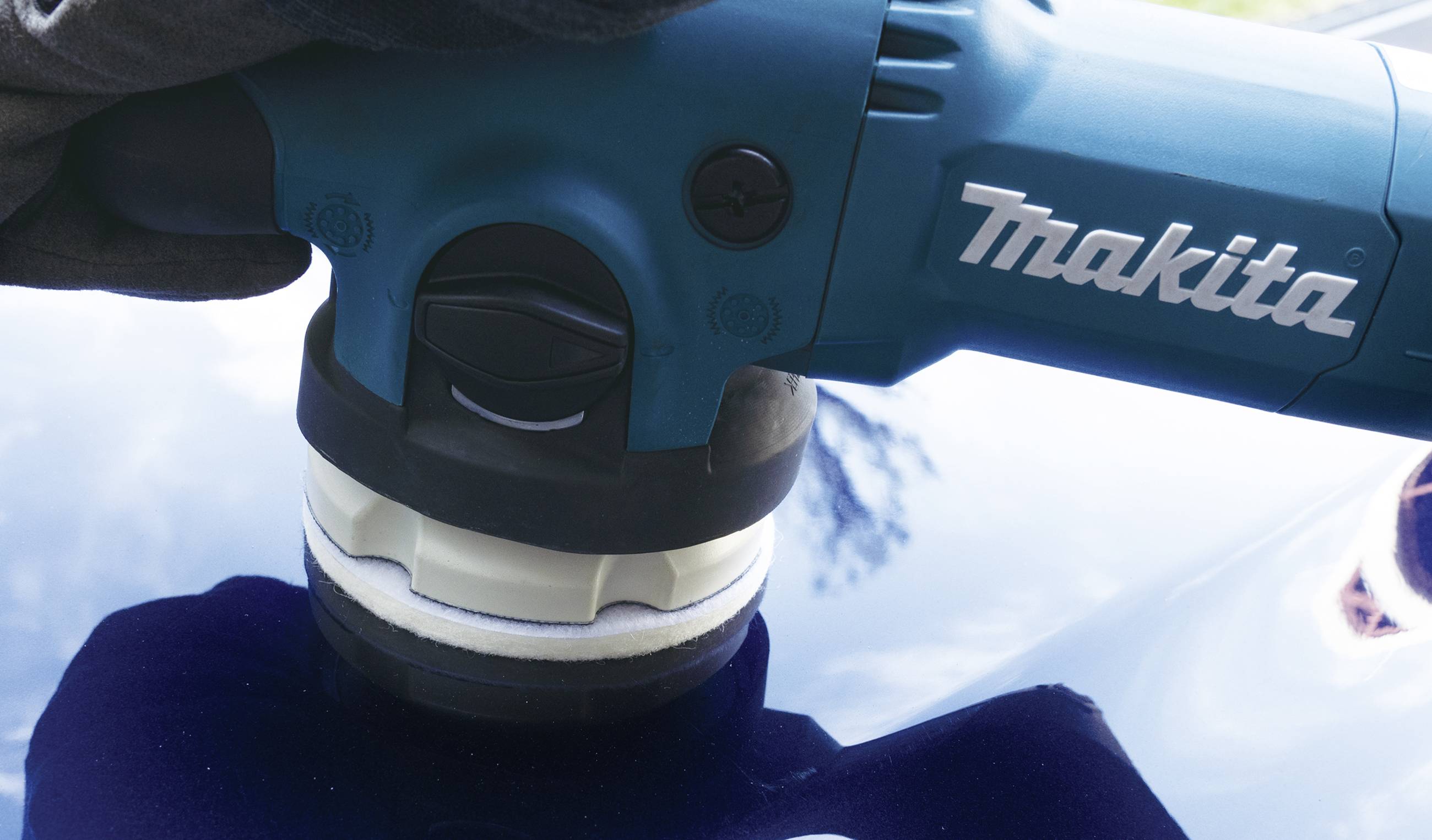 Eine Person poliert die Oberfläche eines Autos mit einer blauen elektrischen Poliermaschine von Makita.