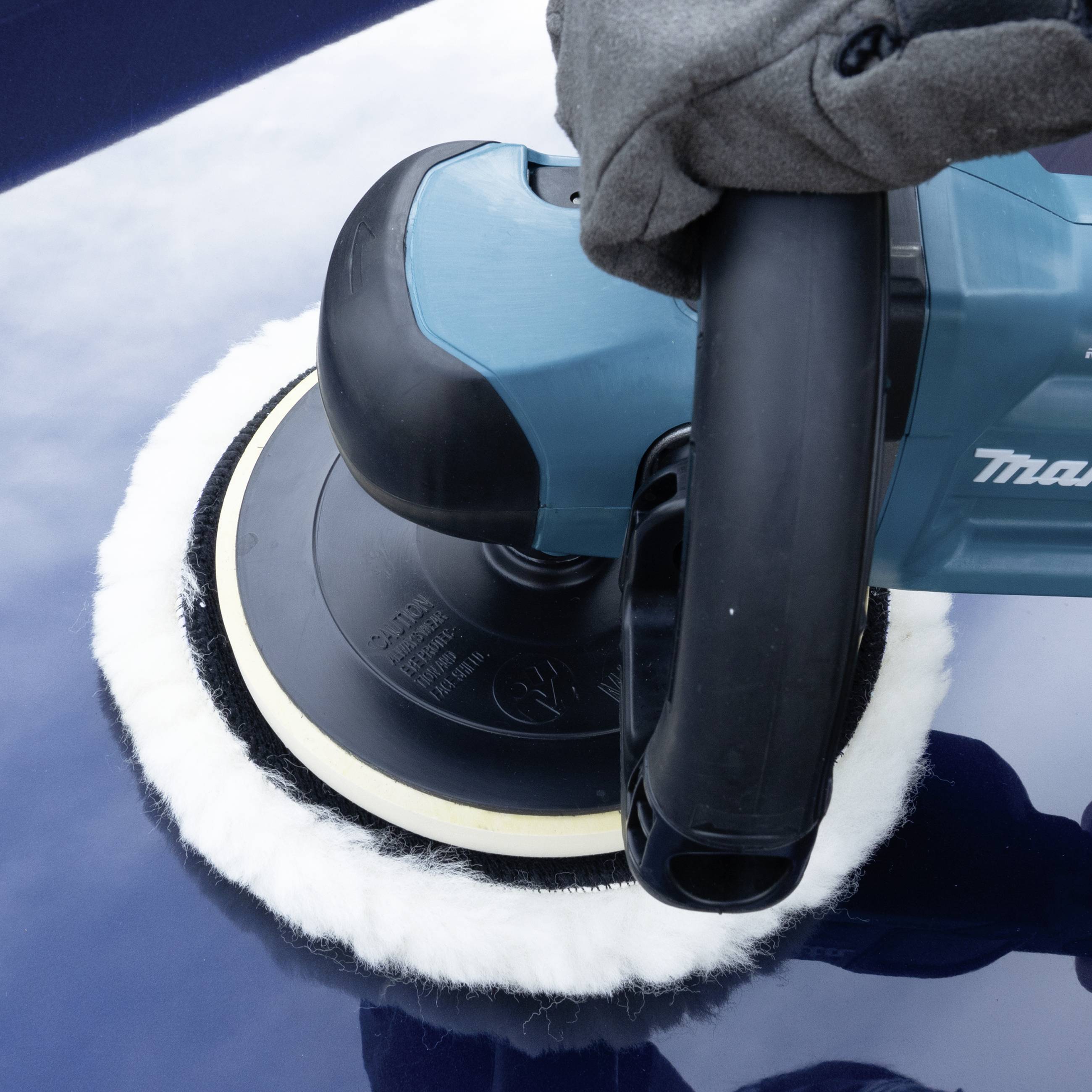 Eine Hand führt eine elektrische Poliermaschine über den blauen Lack eines Autos, um die Oberfläche zu glätten und zu glänzen.