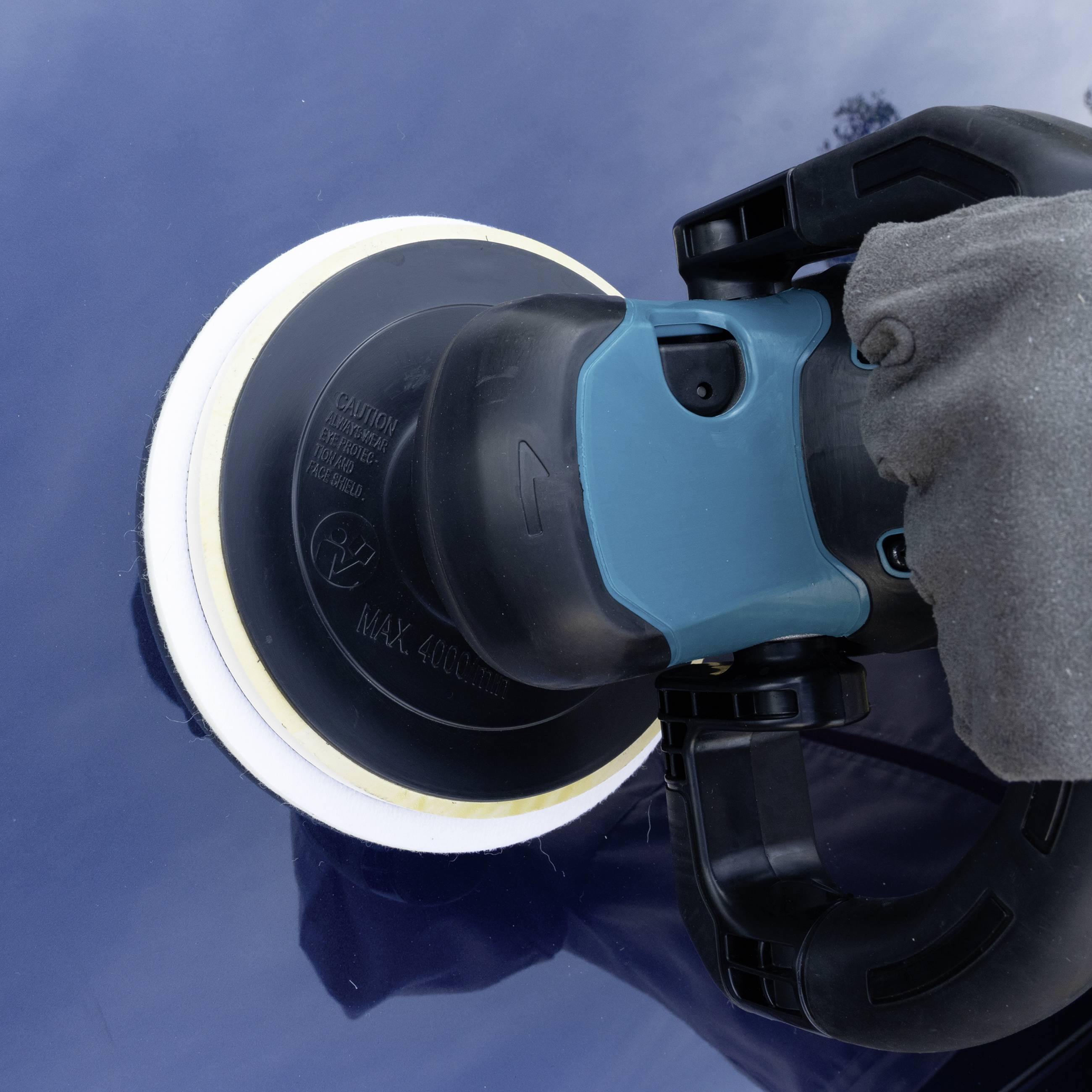 Eine Hand hält eine Poliermaschine auf einer blauen Autolackoberfläche, um den Lack zu polieren und Glanz zu erzeugen.