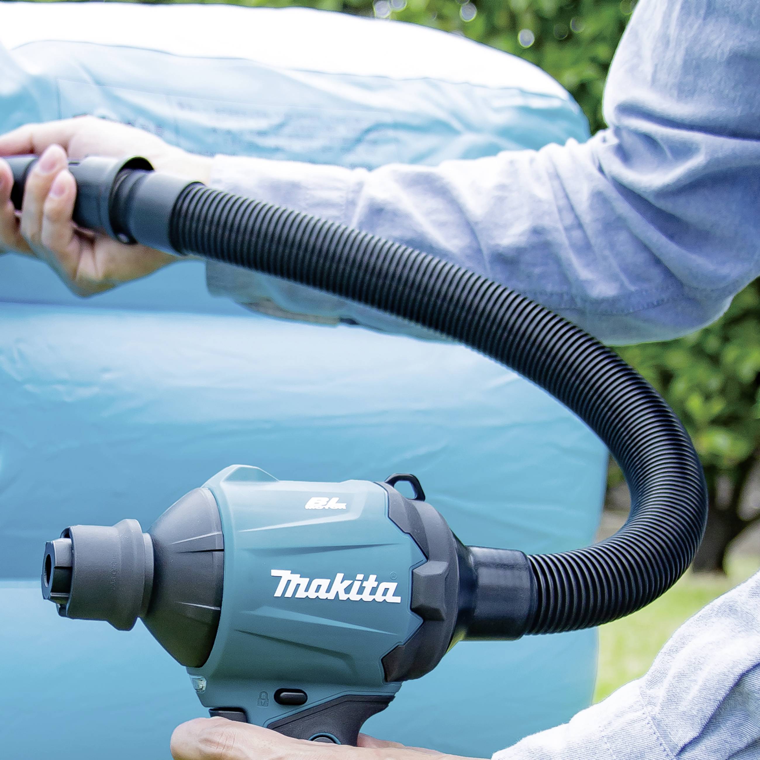 Eine Person hält eine elektrische Luftpumpe und bläst ein großes, blaues aufblasbares Objekt im Freien auf.