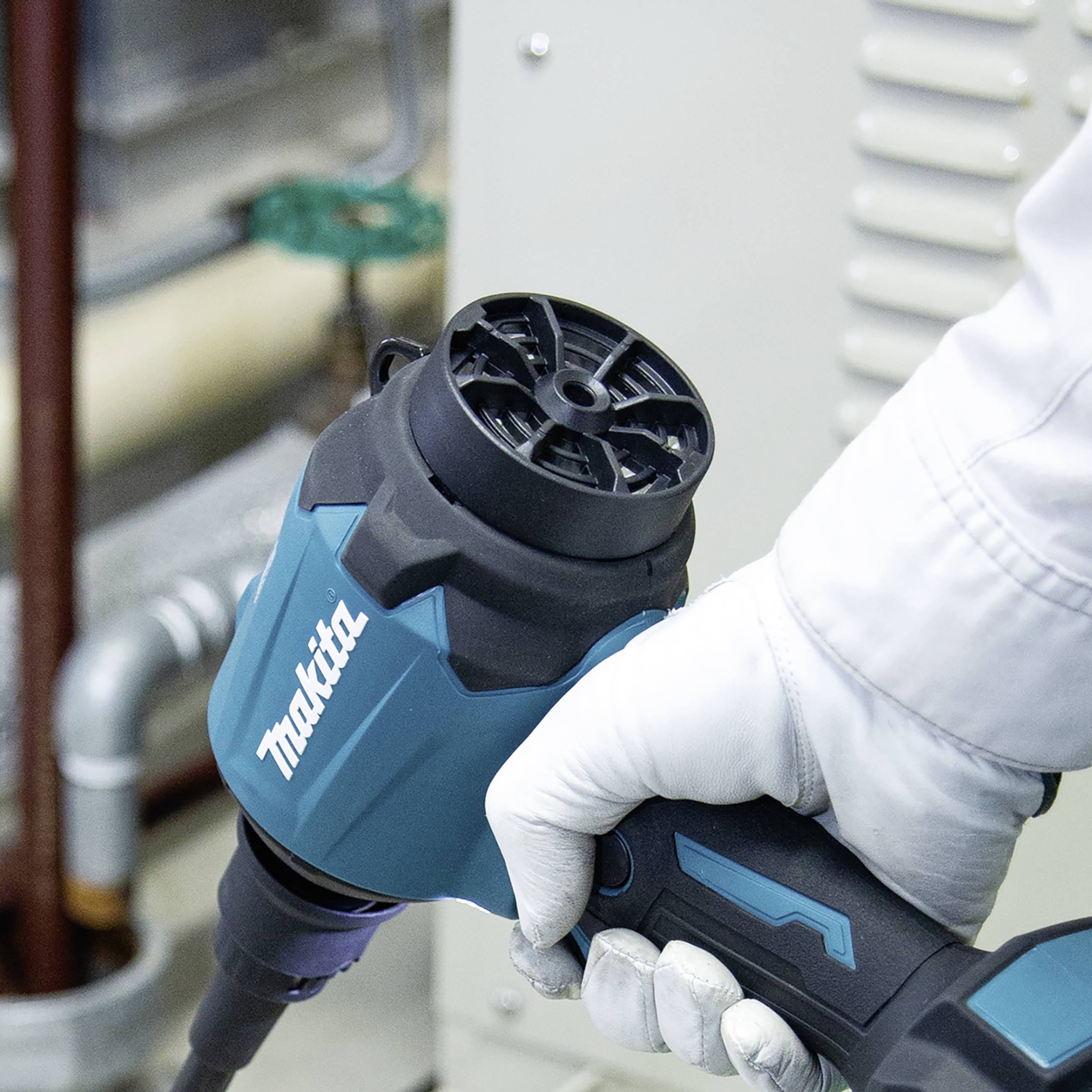 Eine Hand hält ein blau-schwarzes Elektrowerkzeug mit 'Makita'-Logo, vor einem metallischen Hintergrund.