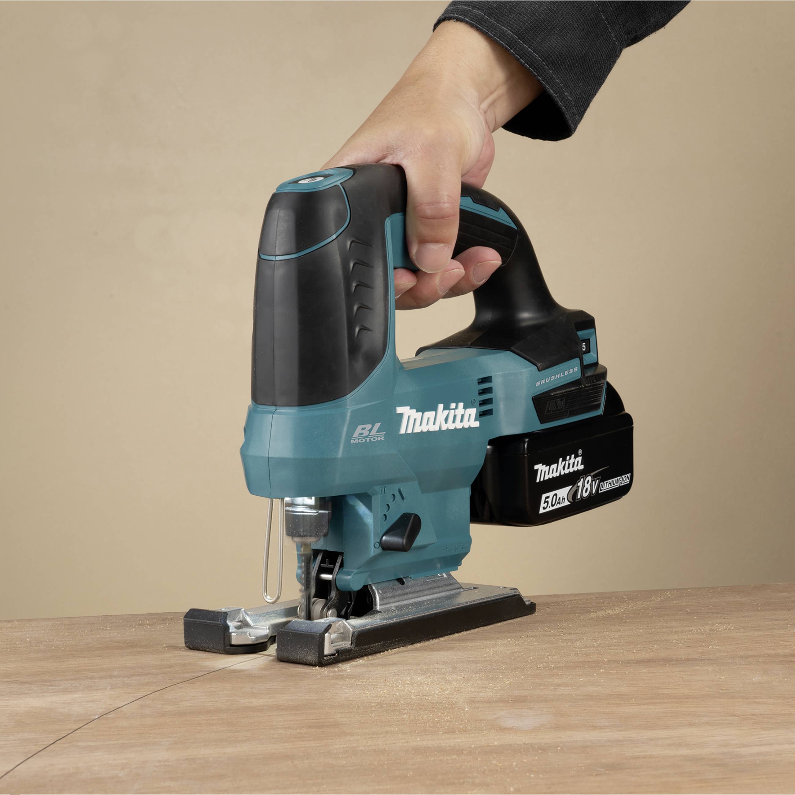 Eine Hand hält eine blaue Makita Akku-Stichsäge über eine Holzplatte, bereit zum Schneiden. Die Säge ist kabellos und kompakt.