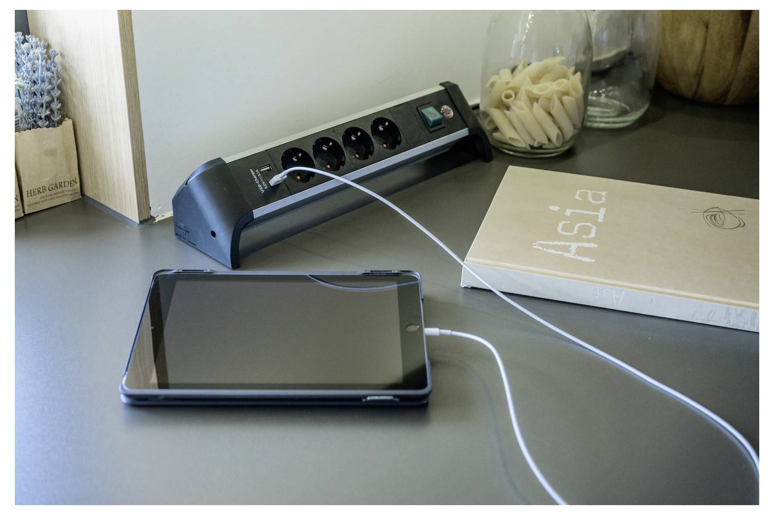 Tablet wird auf einem Schreibtisch neben einer Steckdosenleiste und einem Buch mit dem Titel 