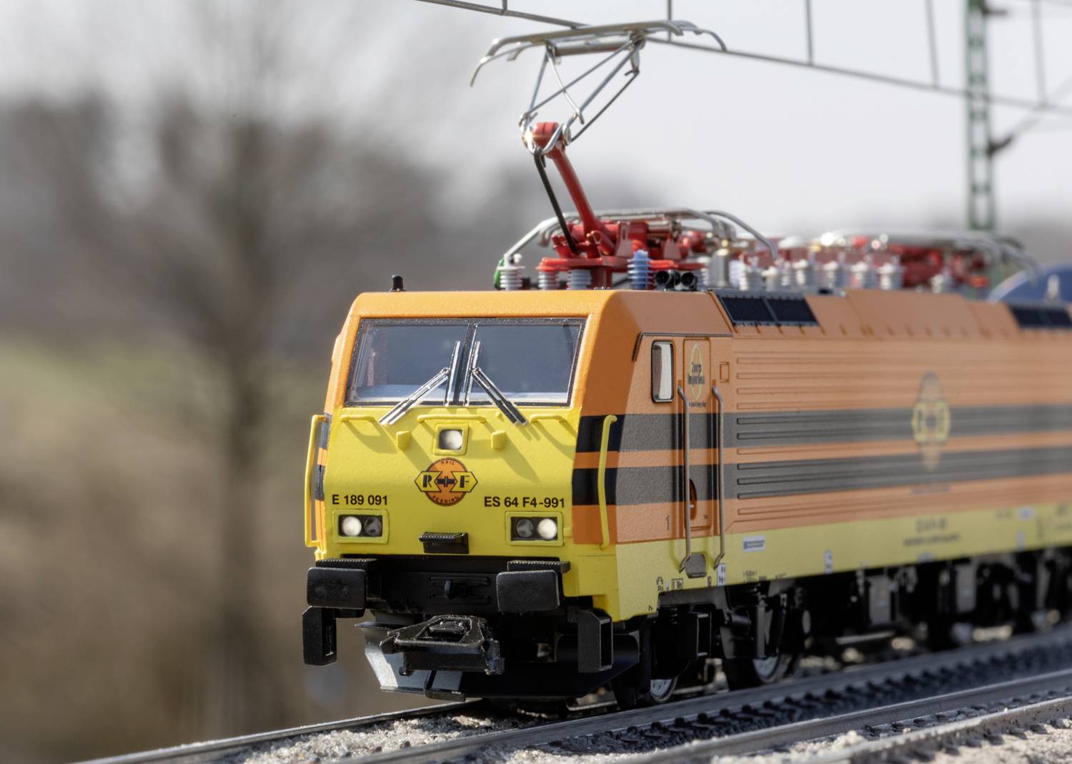 Ein gelb-orangefarbener Zug fährt auf Schienen, umgeben von unscharfem Landschaftshintergrund. Zug trägt das Logo 'PKP Cargo'.