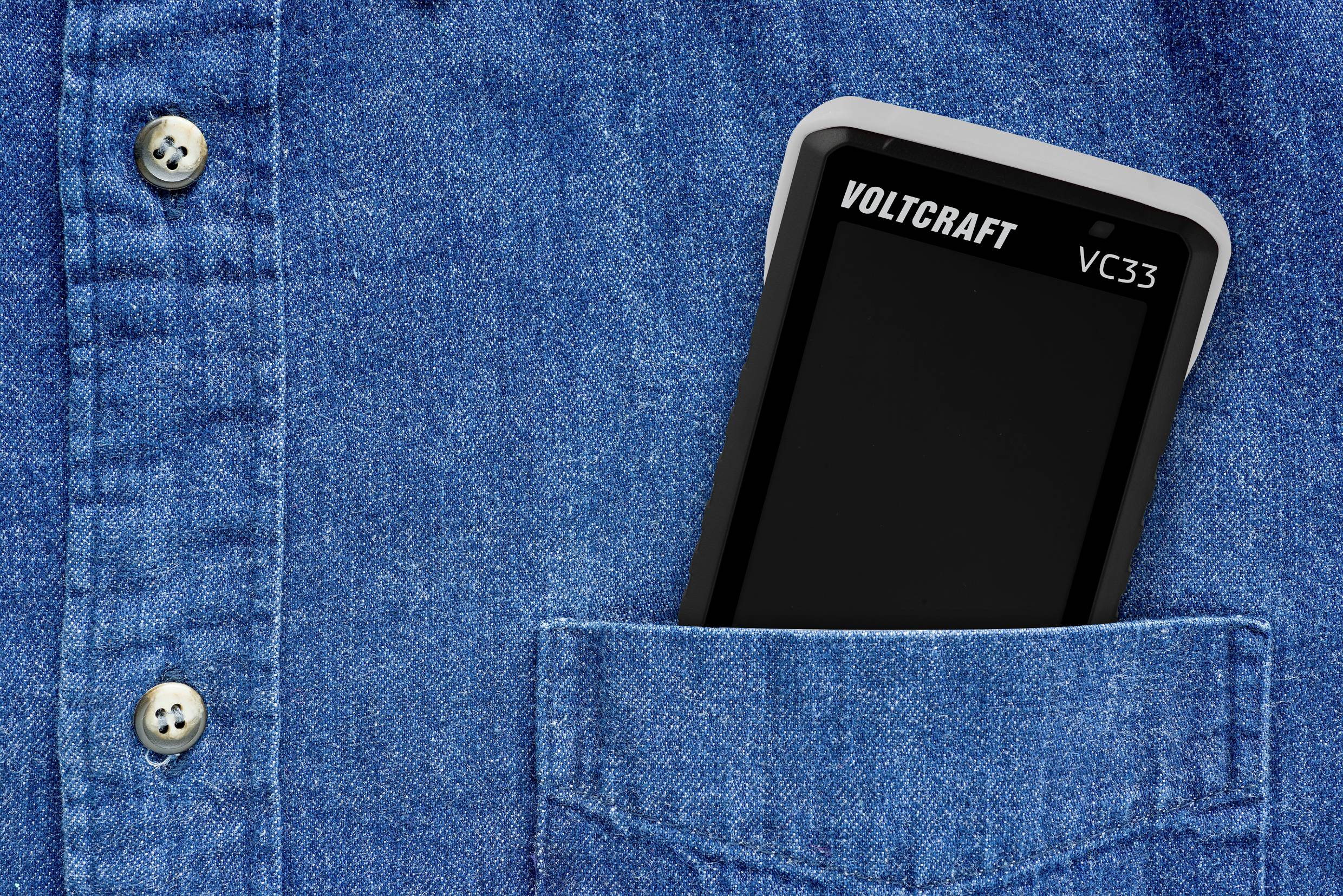 Multimeter steckt in einer blauen Hemdtasche. Nur die obere Hälfte des Geräts ist sichtbar. Der Markenname 'Voltcraft VC33' ist erkennbar.