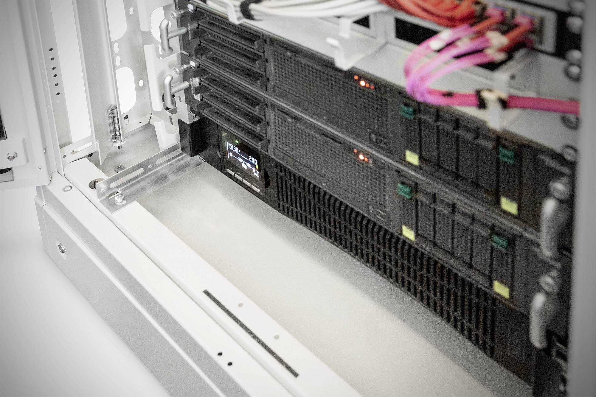Offener Server-Schrank mit mehreren installierten Servern und leuchtenden LED-Anzeigen. Mehrere bunte Kabel sind verbunden.