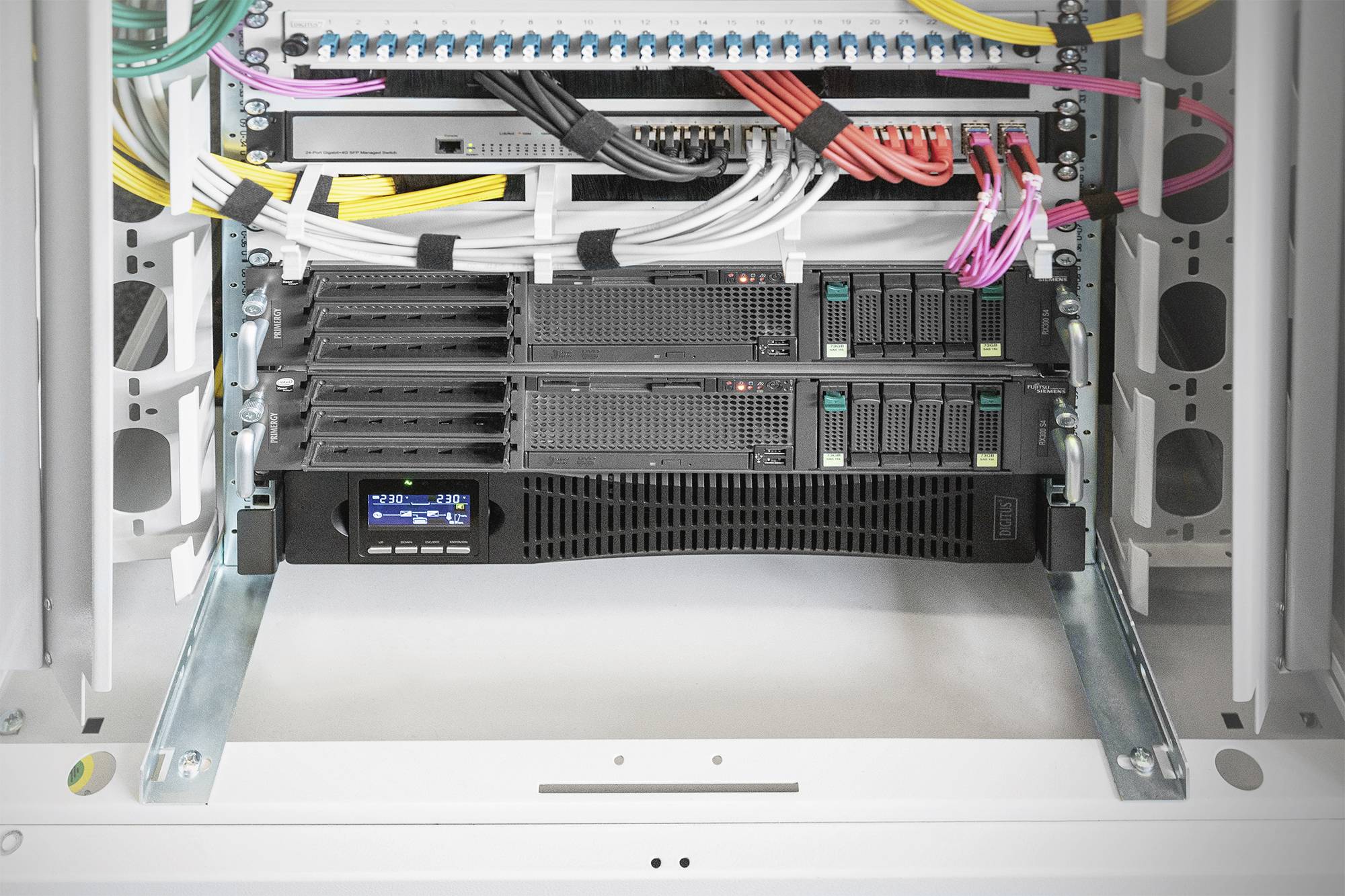 Ein offener Server-Rack mit verschiedenen miteinander verbundenen Kabeln. Zwei Servereinheiten sind montiert, Kabel sind ordentlich organisiert.