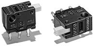 Zwei schwarze Mikroschalter mit drei Anschlussstiften und markierter Beschriftung 'NO', 'NC', 'COM'. Geeignet für elektronische Anwendungen.