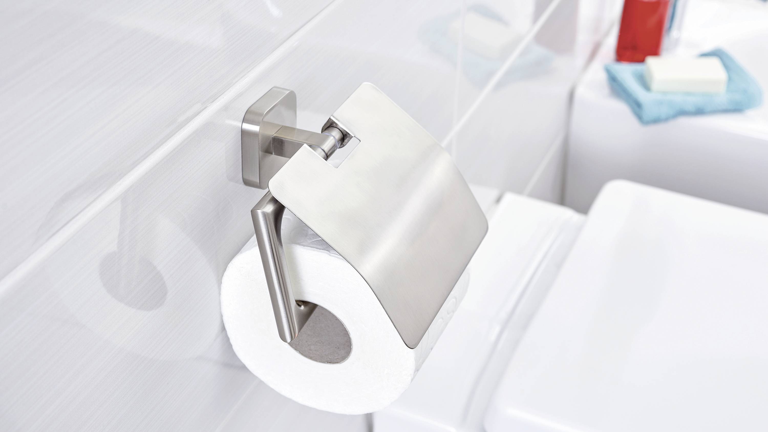 Toilettenpapierrolle in einem modernen Badezimmer, befestigt an einer Metallhalterung an der Wand. Im Hintergrund sind Badutensilien sichtbar.