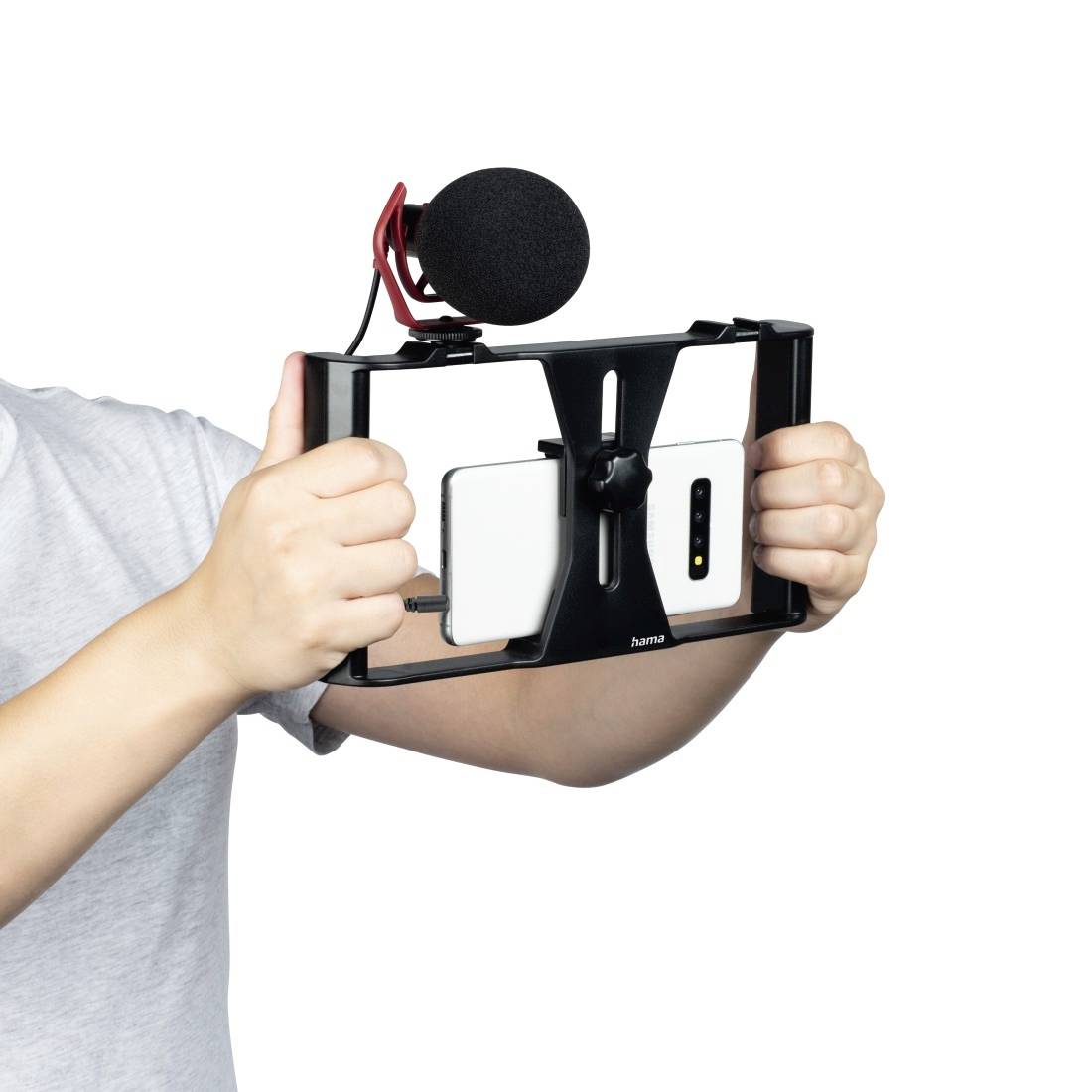 Eine Person hält ein Smartphone in einem stabilisierenden Halter mit einem Mikrofon, geeignet für Videodrehs oder Vlogs.