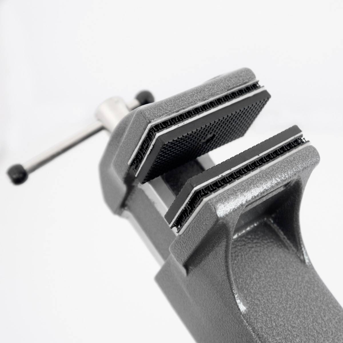 Eine graue Werkbankschraubzwinge aus Metall mit einem Griff an der Rückseite, geöffnet, um ein Objekt zu halten. Vor weißem Hintergrund.