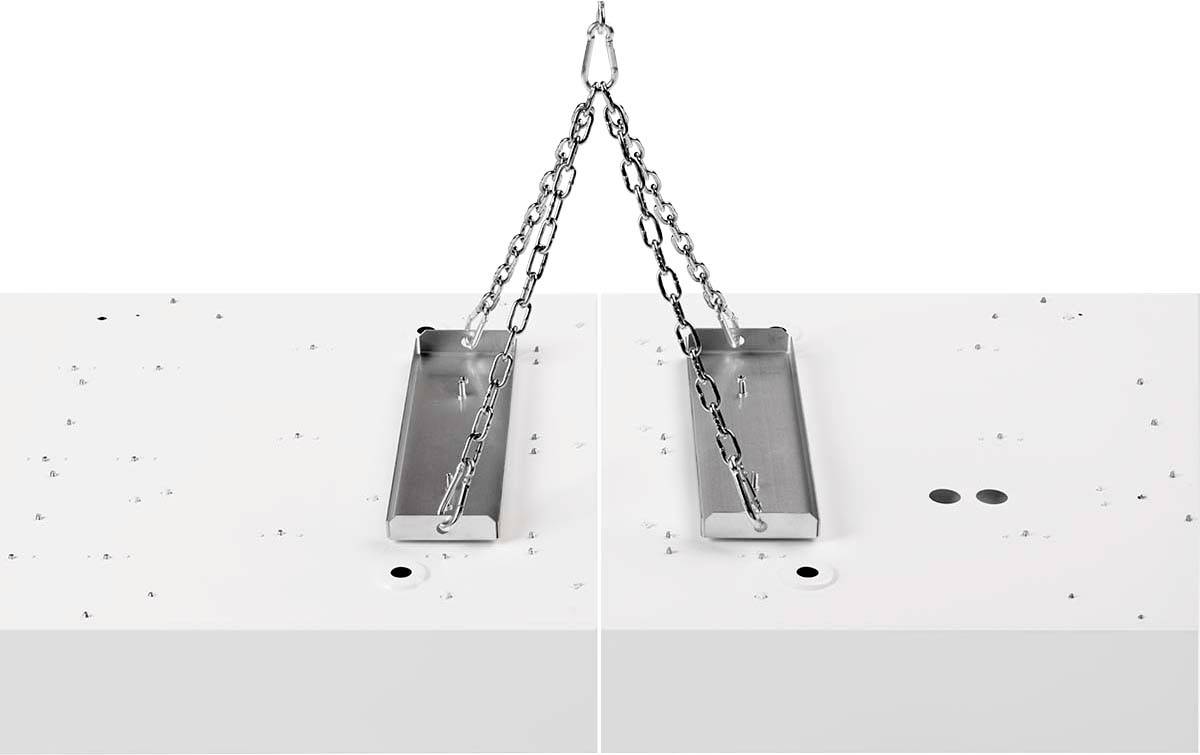 Metallplatte hängt an Ketten über einer weißen Oberfläche mit kleinen schwarzen Punkten.