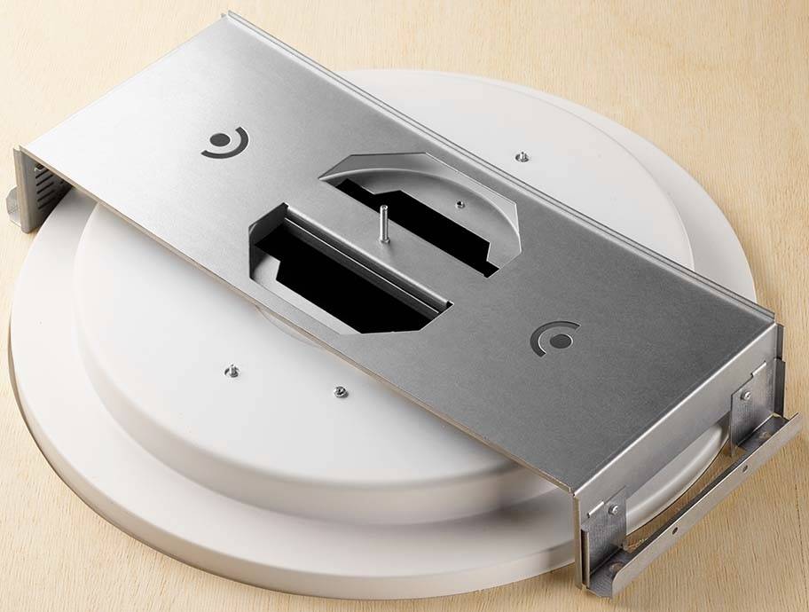 Ein rundes weißes Bauteil mit einem darüber liegenden silbernen Metallrahmen, wahrscheinlich ein Halterungssystem oder Gehäuseelement.