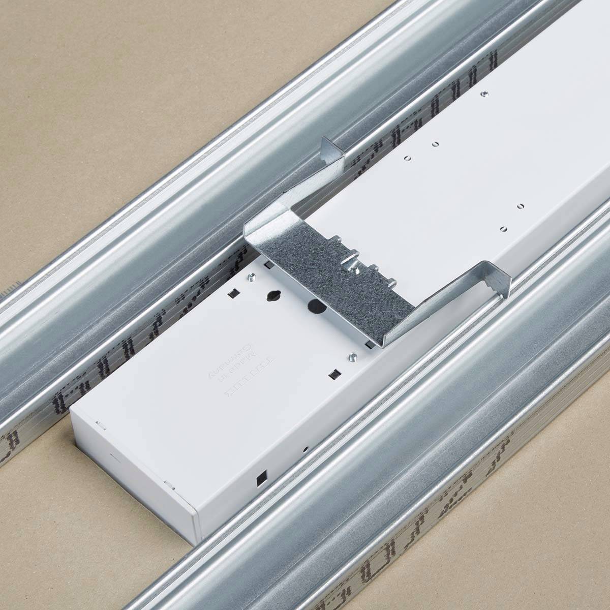 Ein weißer Kabelkanal aus Metall in einer Decke montiert, mit zwei parallel verlaufenden Schienen, auf beigem Hintergrund.