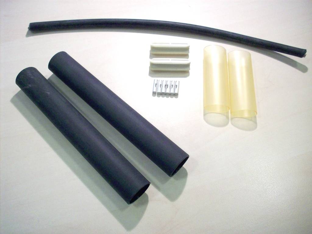 Schwarze und gelbe Schrumpfschläuche, Metallkontakte und Plastikhalterungen liegen auf einer weißen Oberfläche. Elektroinstallationsmaterial.