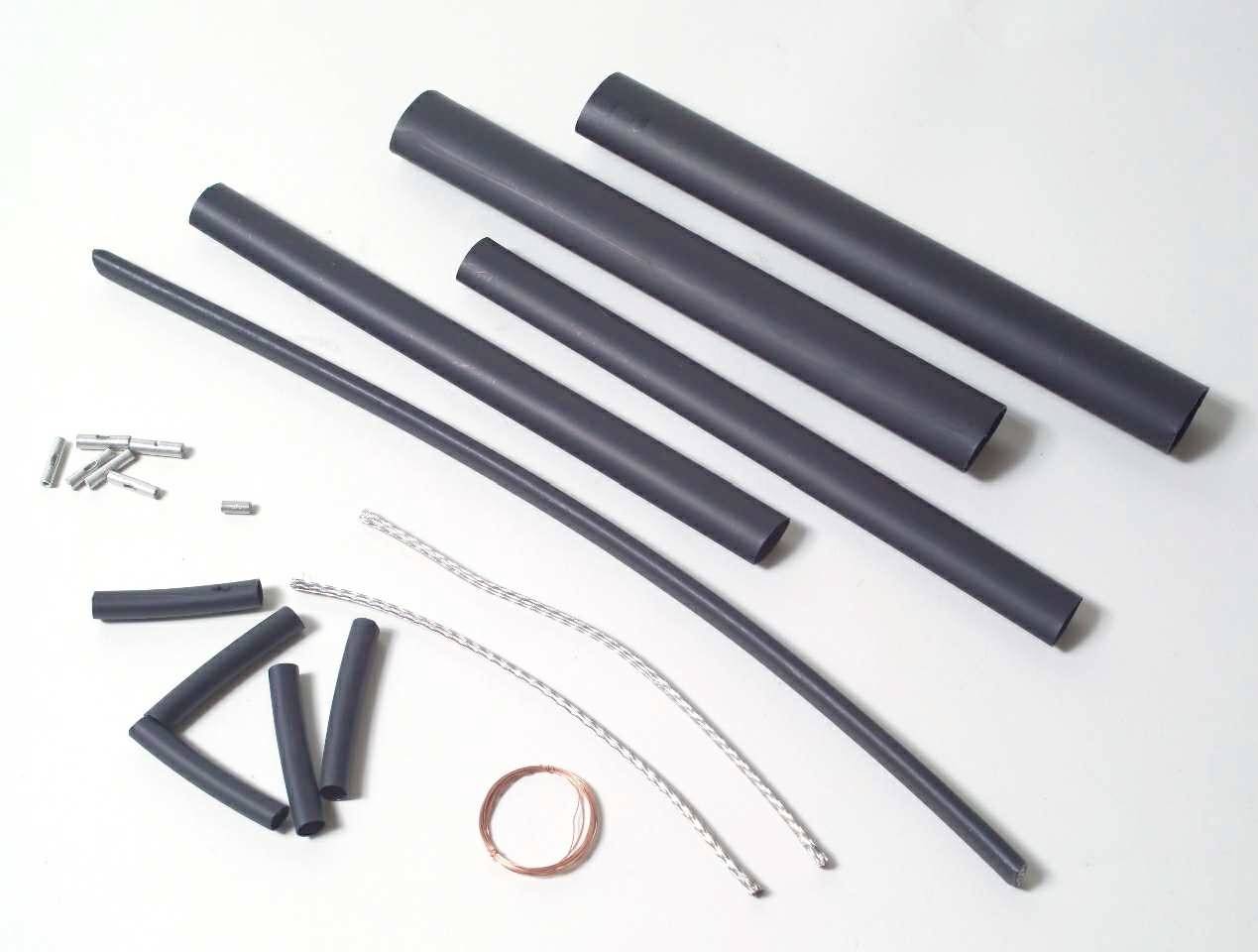 Verschiedene schwarze Schrumpfschläuche und Metallteile auf einer weißen Oberfläche, zur elektrischen Isolierung und Verbindung.