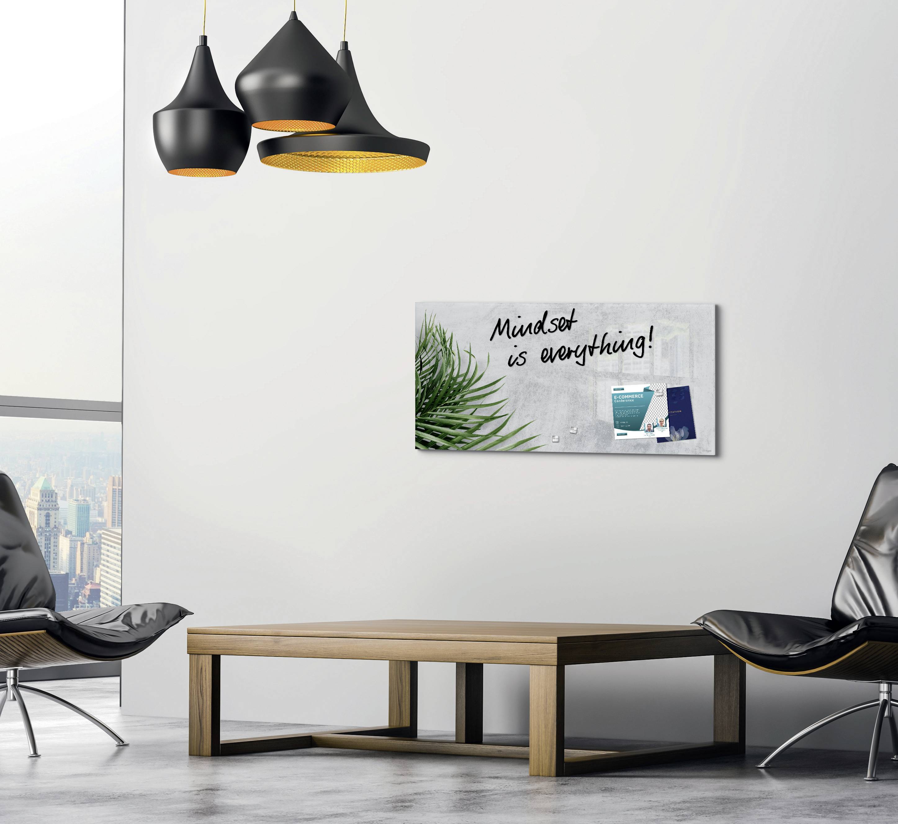 Ein Wohnzimmer mit modernen schwarzen Lampen, minimalistischem Holztisch und grauem Stuhl. An der Wand ein Bild mit der Aufschrift 'Mindset is everything!', einem Blatt und Bürobedarf.