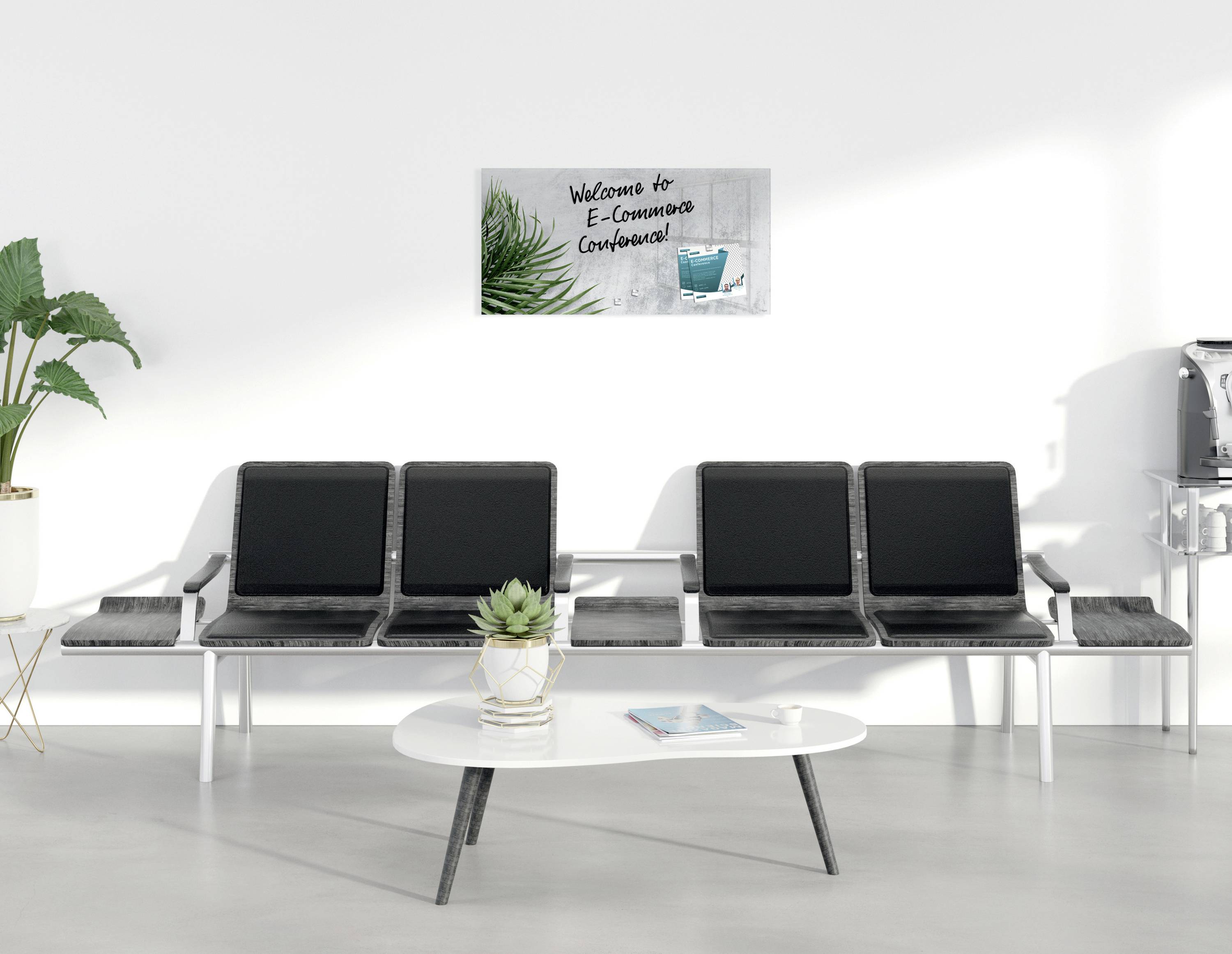 Warteraum mit vier grauen Stühlen, einem Tisch und Pflanzen. An der Wand ein Schild mit der Aufschrift 'Welcome to E-Commerce Conference'.