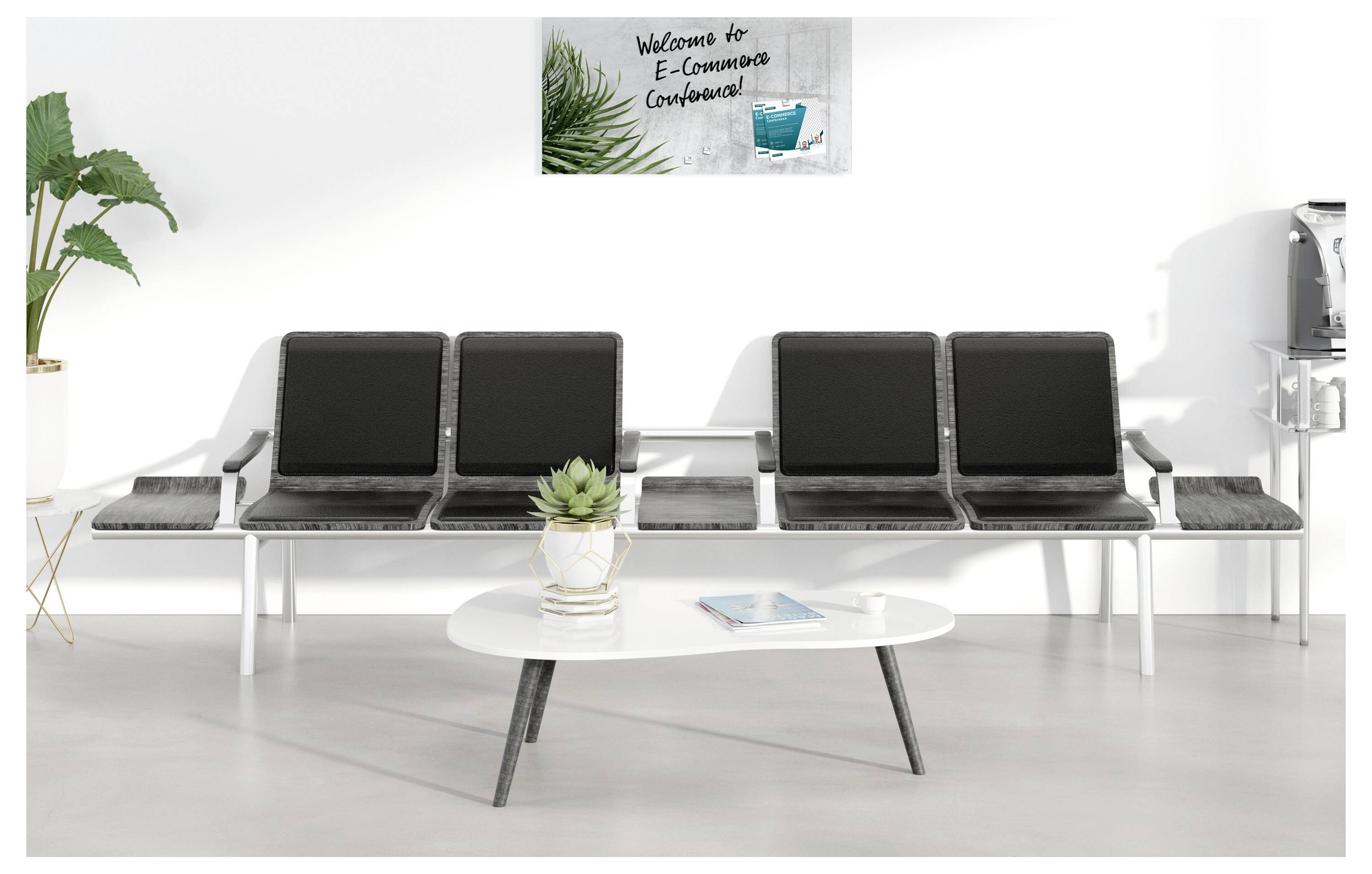 Moderner Wartbereich mit vier schwarzen Stühlen, Beistelltischen, einem Couchtisch, Pflanzen und einem Schild mit der Aufschrift „Willkommen zur E-Konsultations-Konferenz".