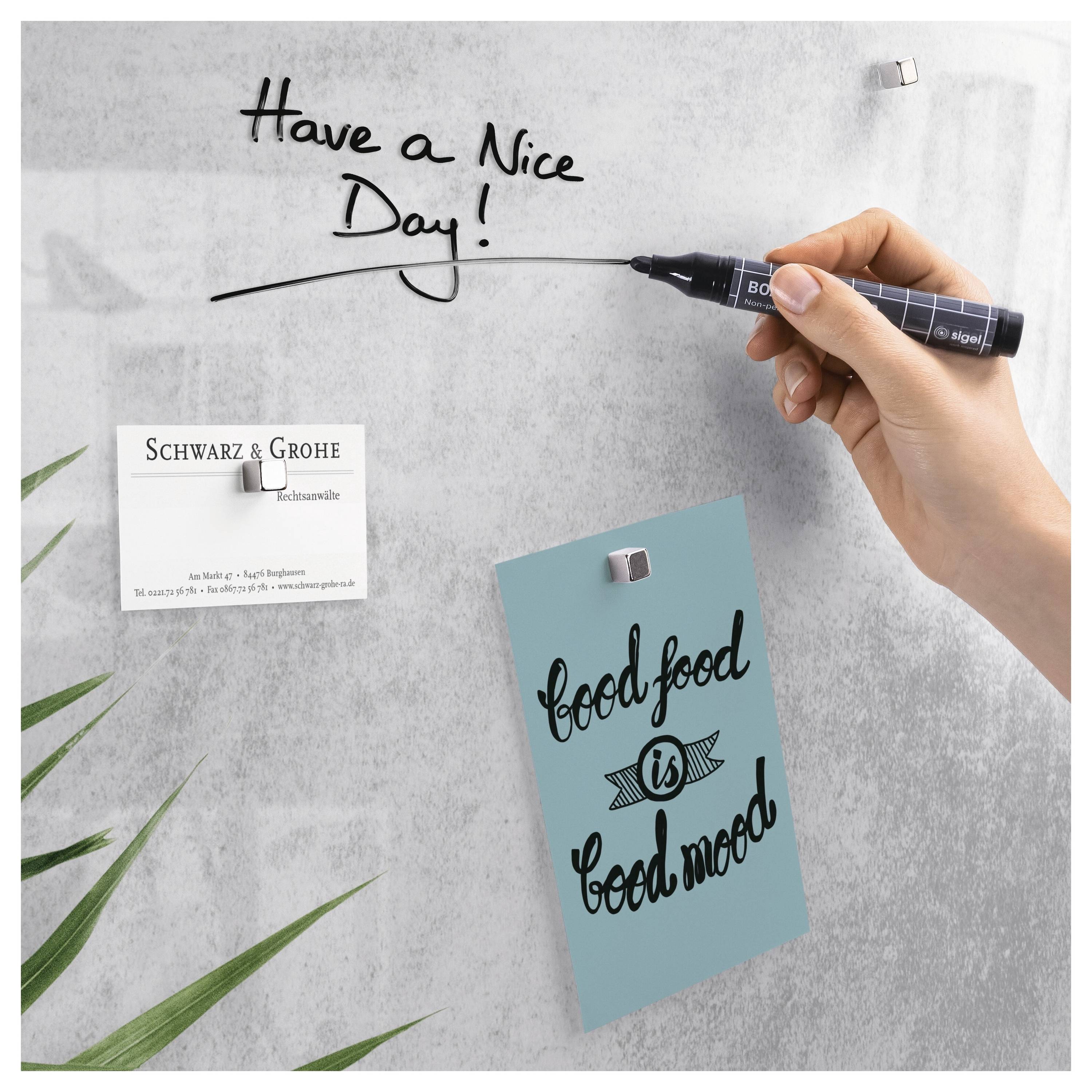 Eine Hand schreibt "Have a Nice Day!" auf ein Whiteboard neben zwei magnetisch gehaltenen Karten, eine mit der Aufschrift "Schwarz & Grohe" und eine andere mit "food is good mood".