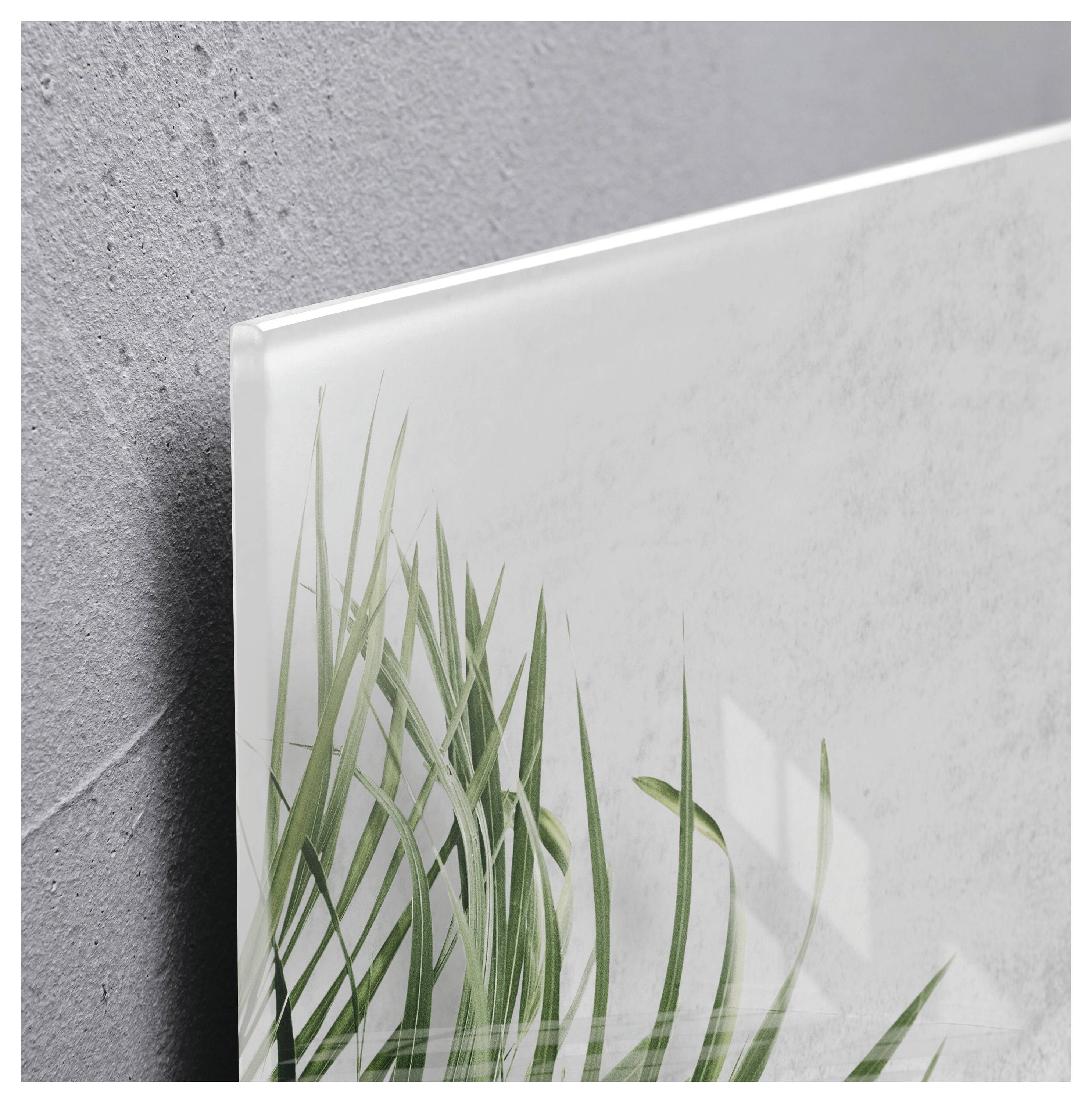 Nahaufnahme eines gerahmten botanischen Drucks mit grünen Grasblättern vor hellem Hintergrund, der neben einer strukturierten grauen Wand lehnt.