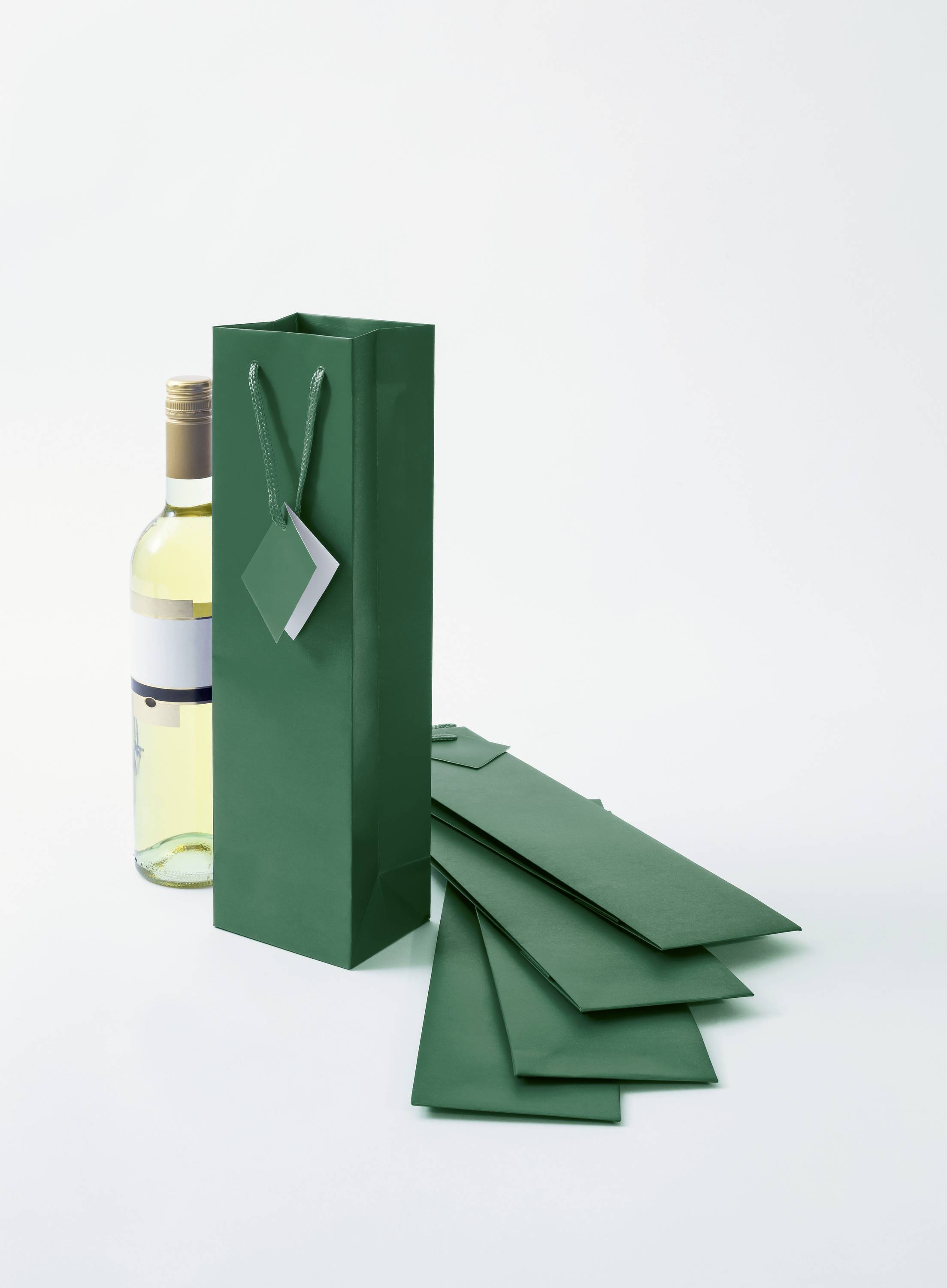 Grüne Geschenktüte neben einer Weinflasche auf hellem Hintergrund.