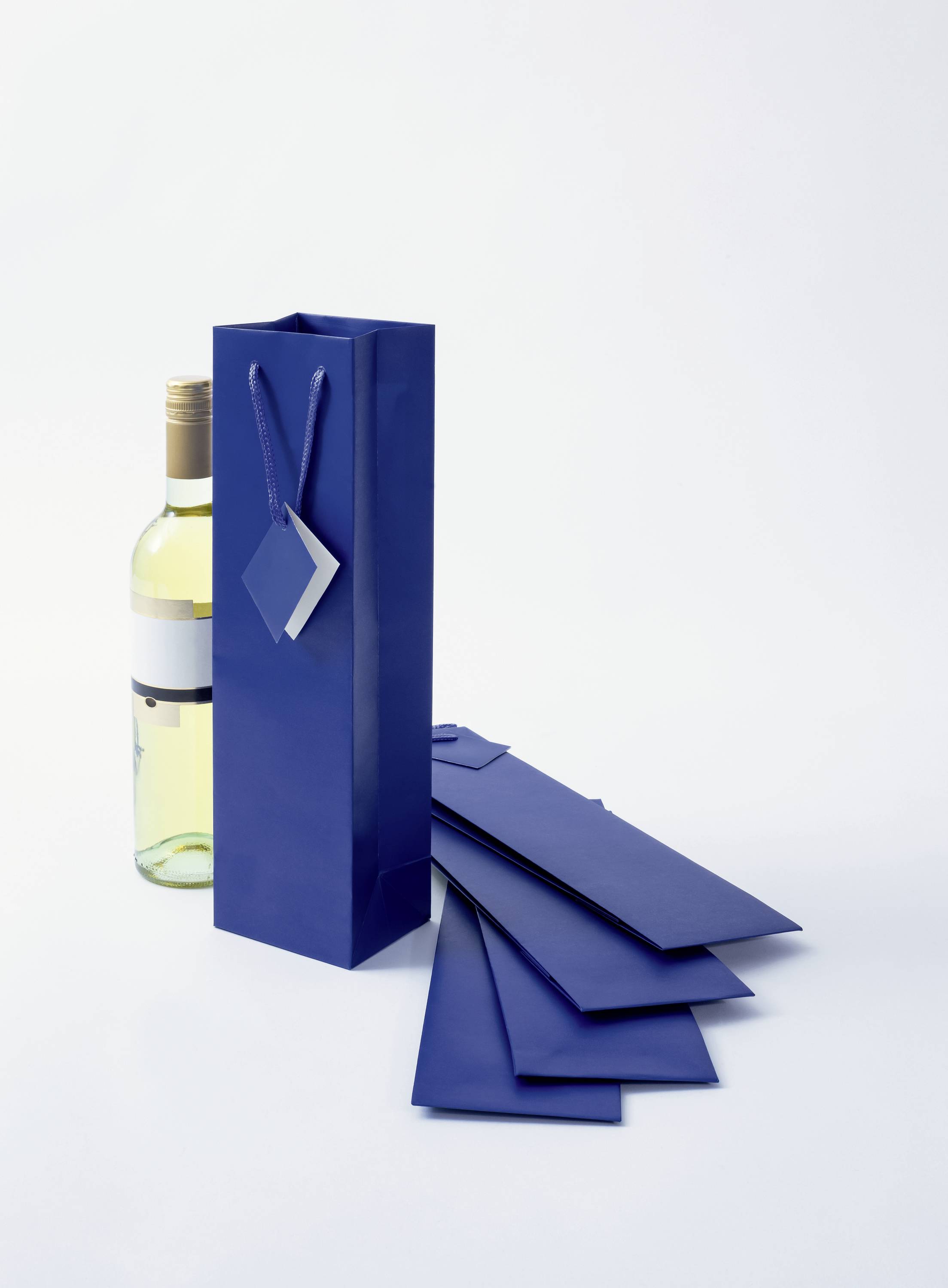 Eine Weinflasche mit Etikett steht neben einer blauen Geschenktasche und mehreren blauen Briefumschlägen auf weißem Hintergrund.