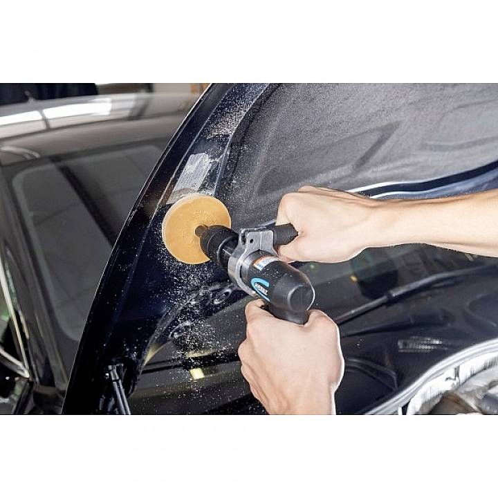 Eine Person poliert den Kotflügel eines schwarzen Autos mit einer Poliermaschine. Es fliegen Polierreste in der Luft.